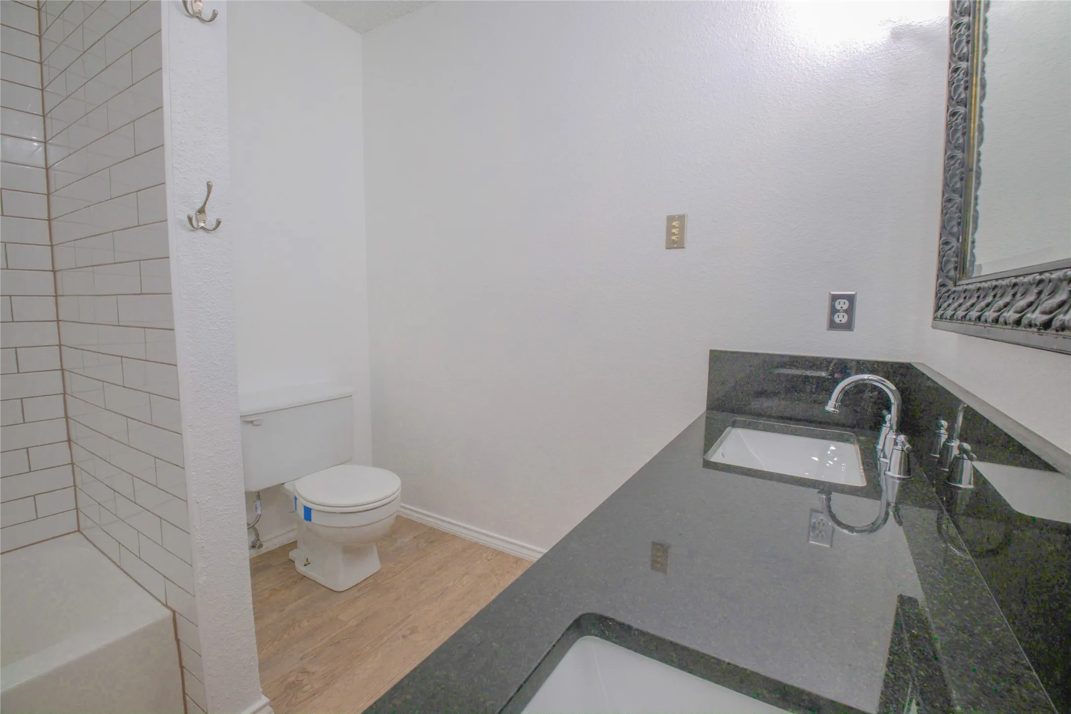 Dual undermount sinks with black stone countertop, chrome fixtures, and wood-finish flooring