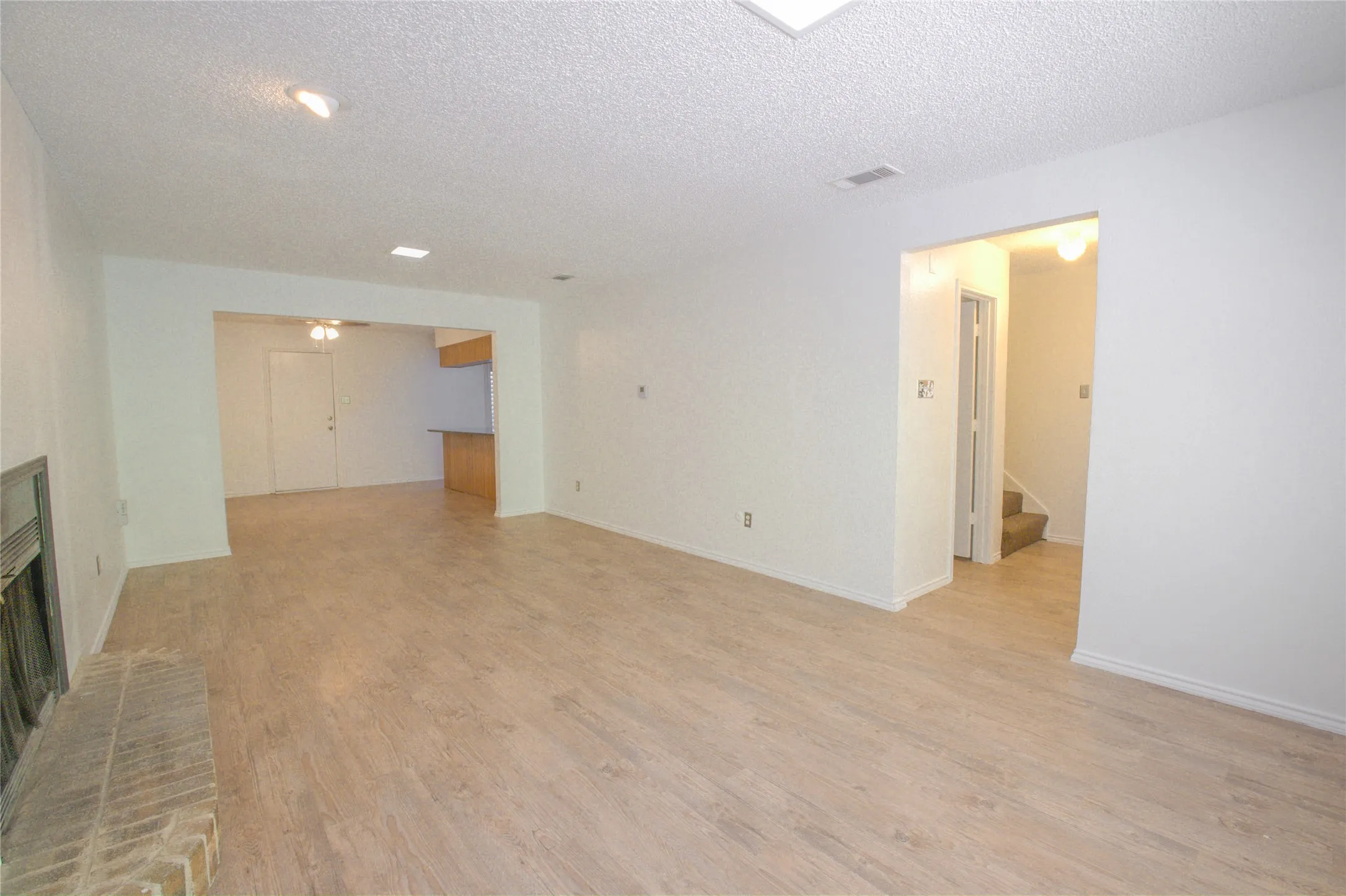 Spacious room featuring wood-finish flooring, a brick-surround fireplace, and recessed lighting