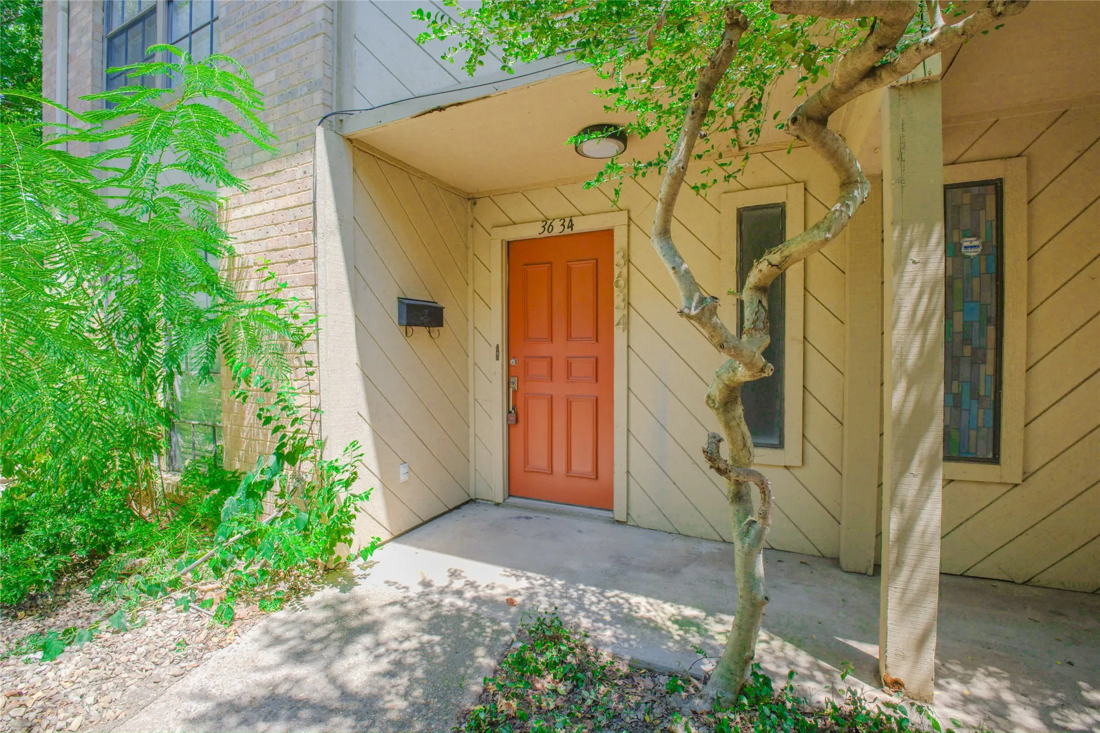 Entry porch with an orange paneled door, diagonal siding, and multi-pane transom windows