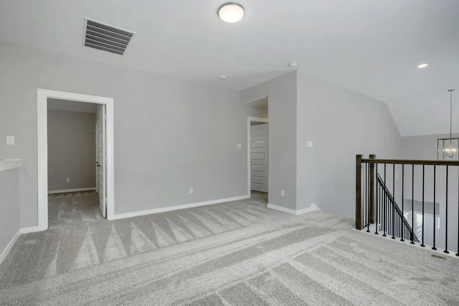 Carpeted upstairs landing with light gray walls, white trim, recessed lighting, and a dark wood and black metal baluster railing