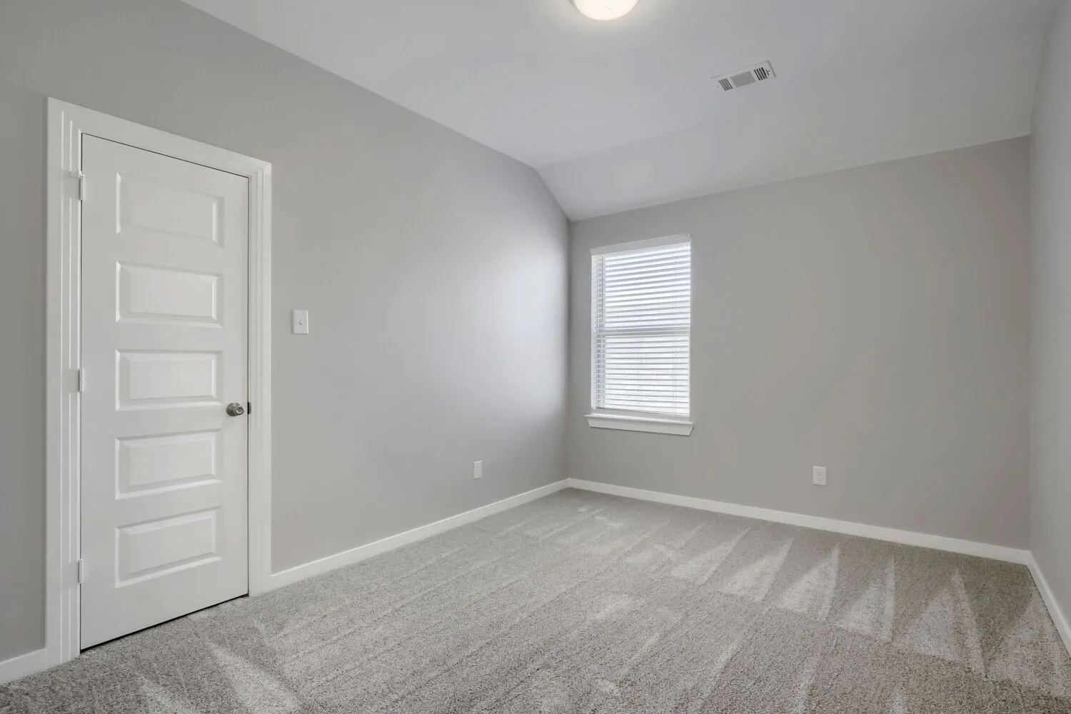 Bright secondary bedroom featuring neutral gray walls, recessed ceiling lighting, carpet flooring, and a large window with plantation shutters allowing natural light