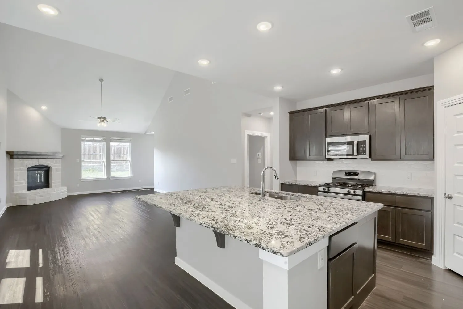 Open-concept kitchen with a large granite island, stainless steel appliances, and dark wood-finish cabinetry