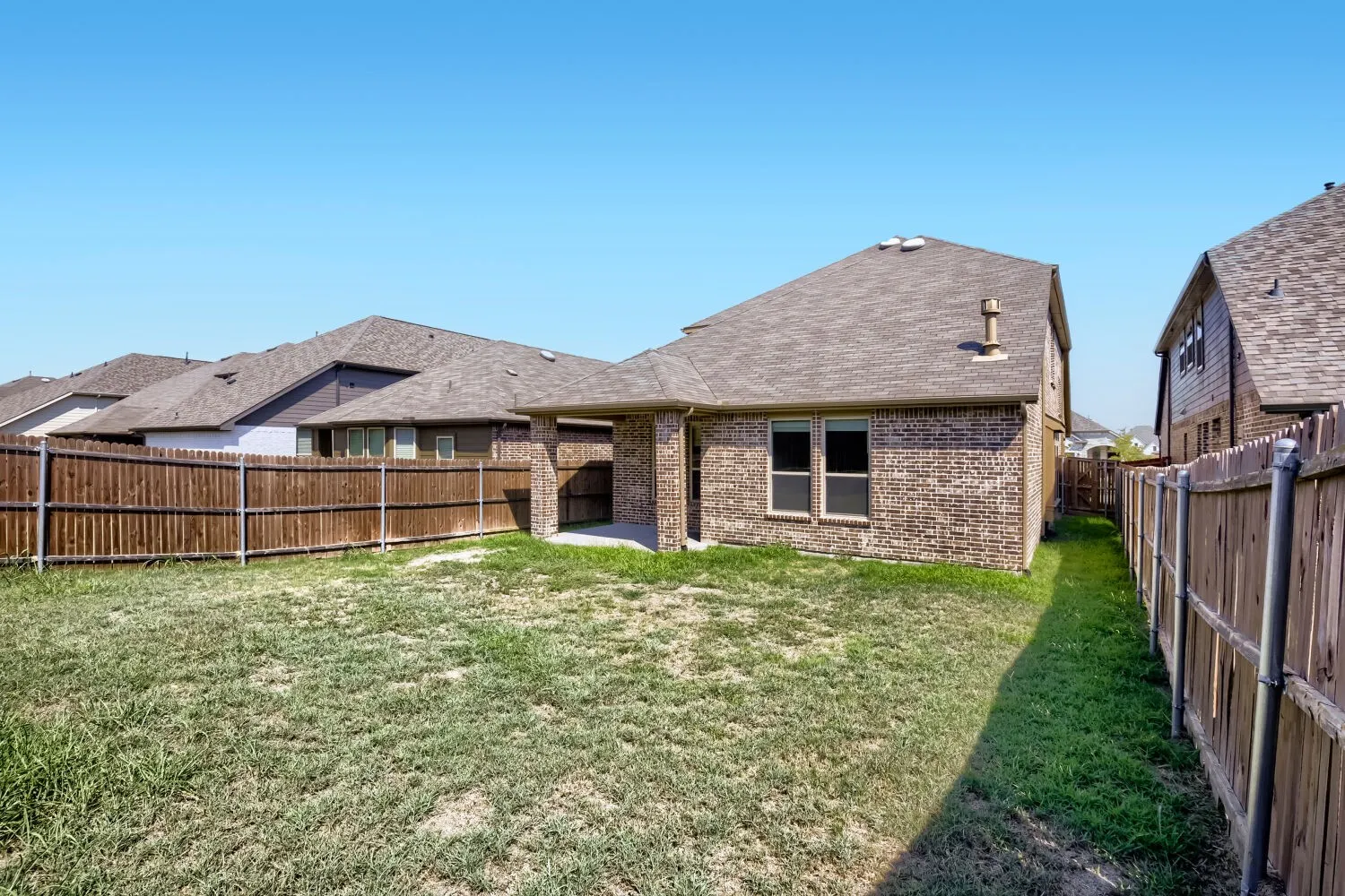 Expansive backyard featuring a privacy fence, brick exterior, and covered patio