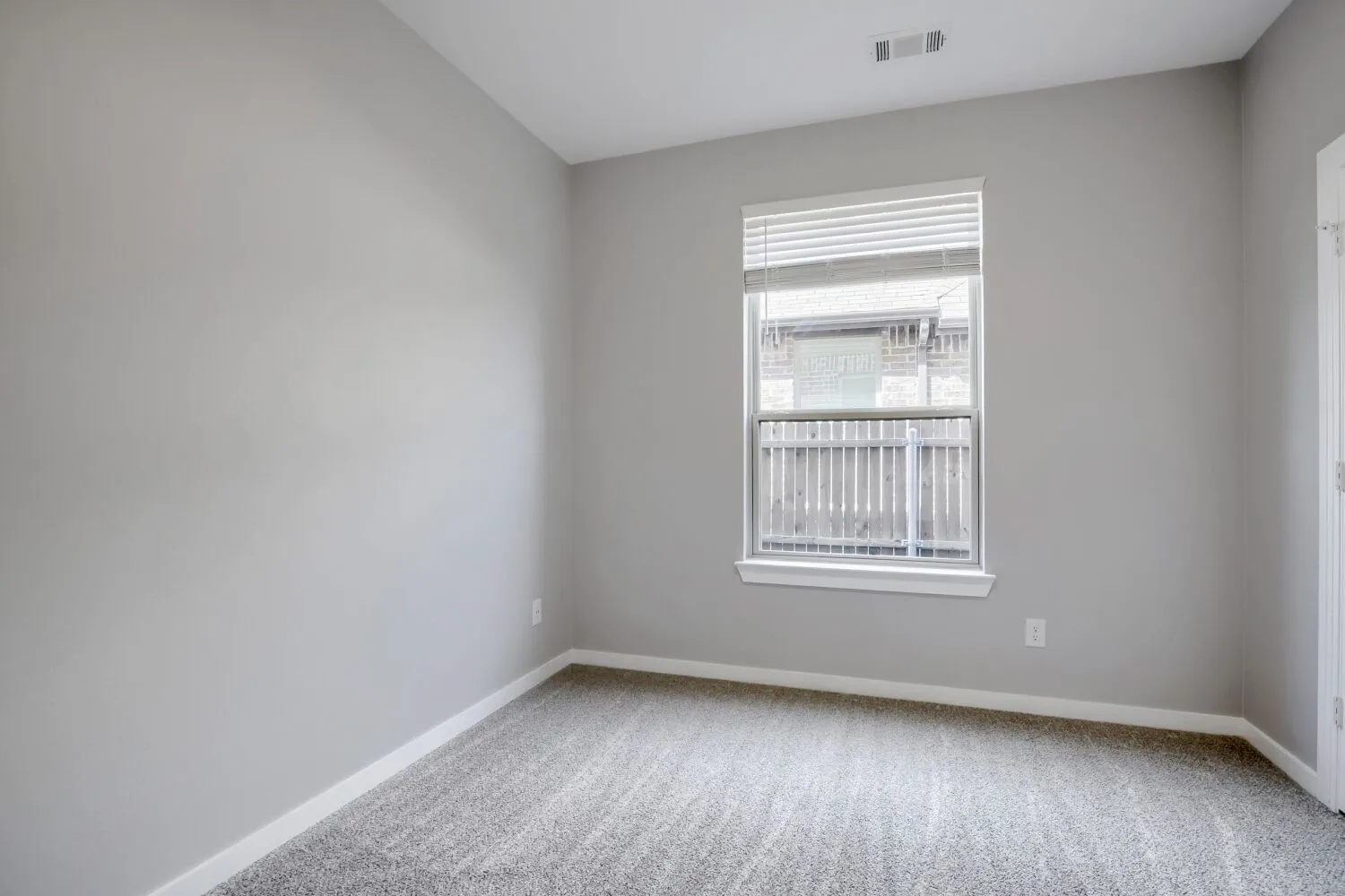 Bright secondary bedroom featuring neutral wall finishes, carpeted flooring, and a large double-hung window with horizontal blinds allowing abundant natural light