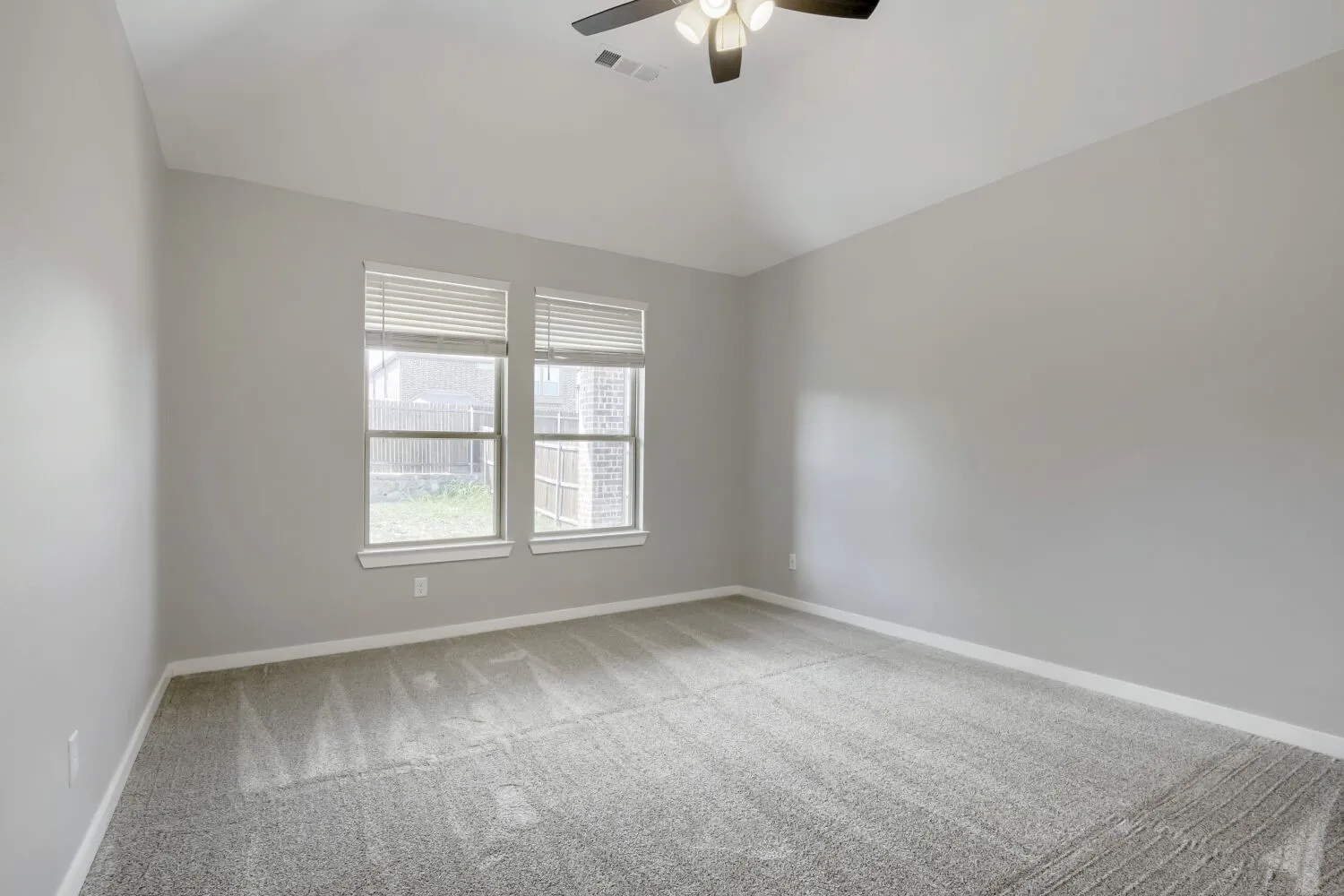 Bright secondary bedroom with expansive windows featuring plantation shutters, neutral gray walls, and plush carpeting throughout