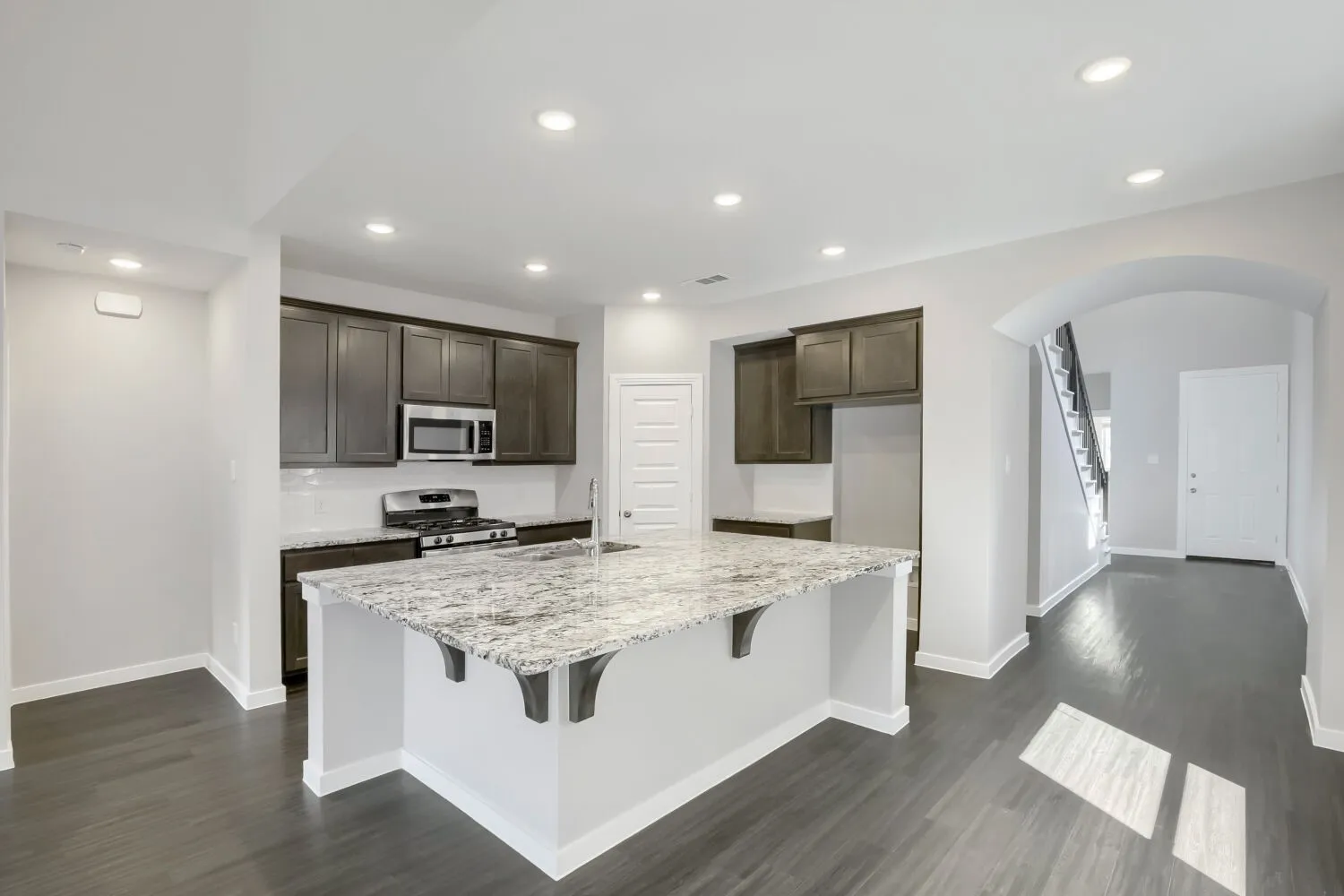 Kitchen featuring a large island with a stone countertop, dark wood-finish cabinetry, stainless steel appliances, and wood-finish flooring