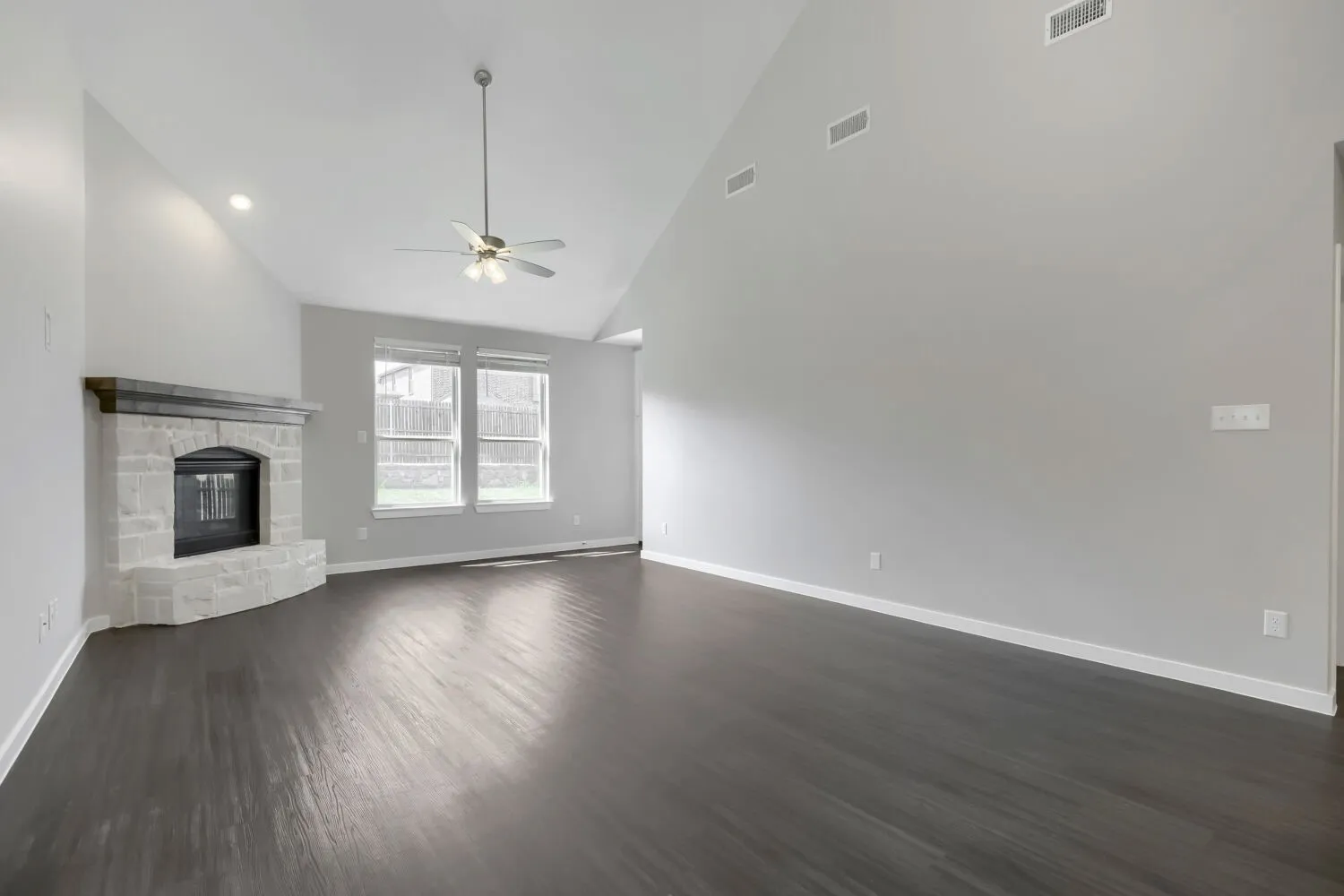 Vaulted ceilings with recessed lighting, stone-clad fireplace, dark wood-finish flooring, and a ceiling fan