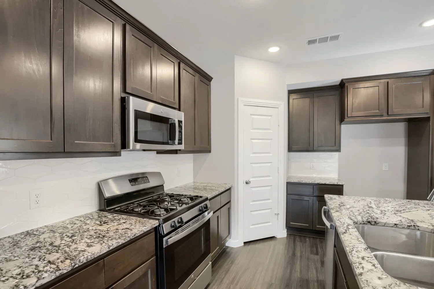 Modern kitchen featuring dark wood cabinetry, granite countertops, stainless steel gas range with overhead microwave, and dual undermount sinks
