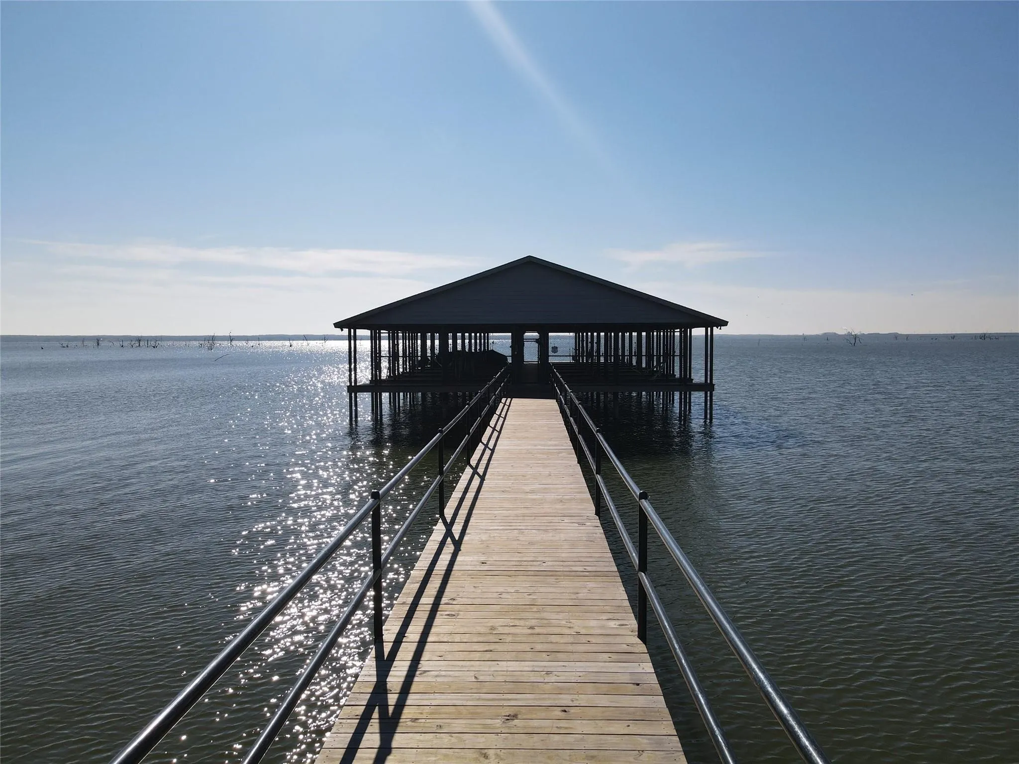 Wood-finish pier with black metal railings leading to a covered boat dock