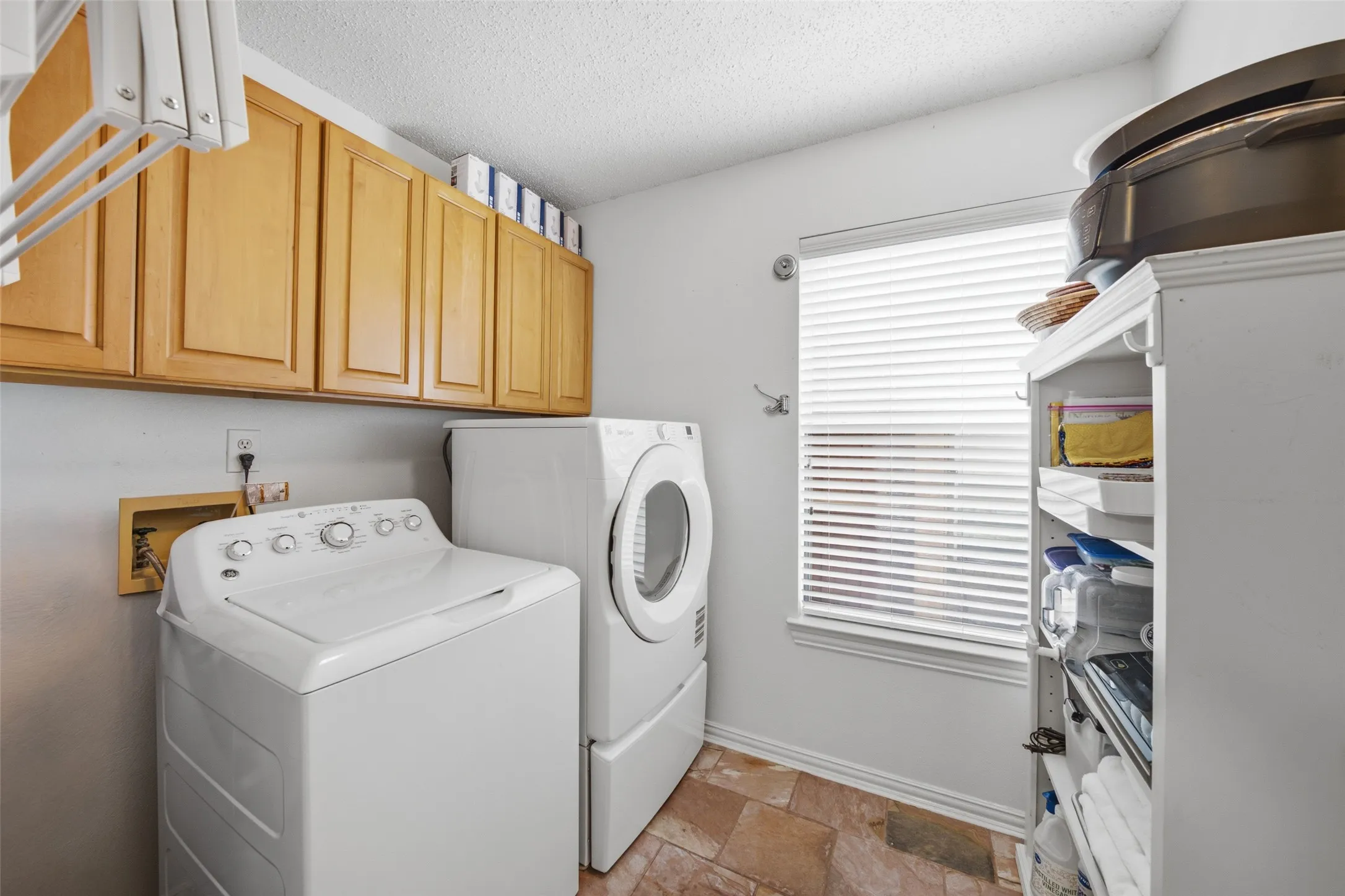Utility room with full-size washer and dryer, upper storage cabinets, and tile flooring — practical and conveniently located.
