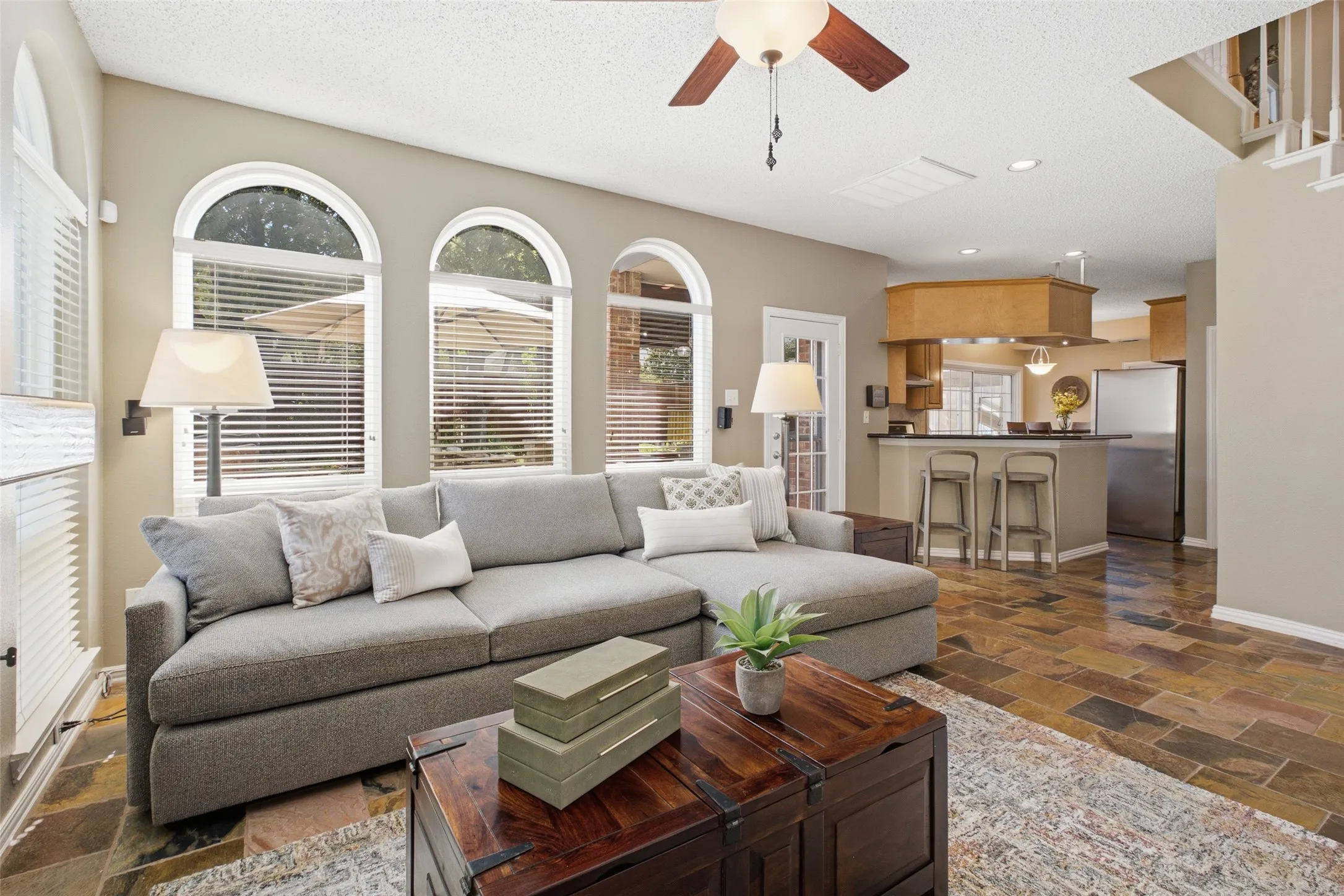Open-concept family room flowing seamlessly into the kitchen and breakfast bar, with arched windows, rich slate tile floors, and a layout built for everyday living.