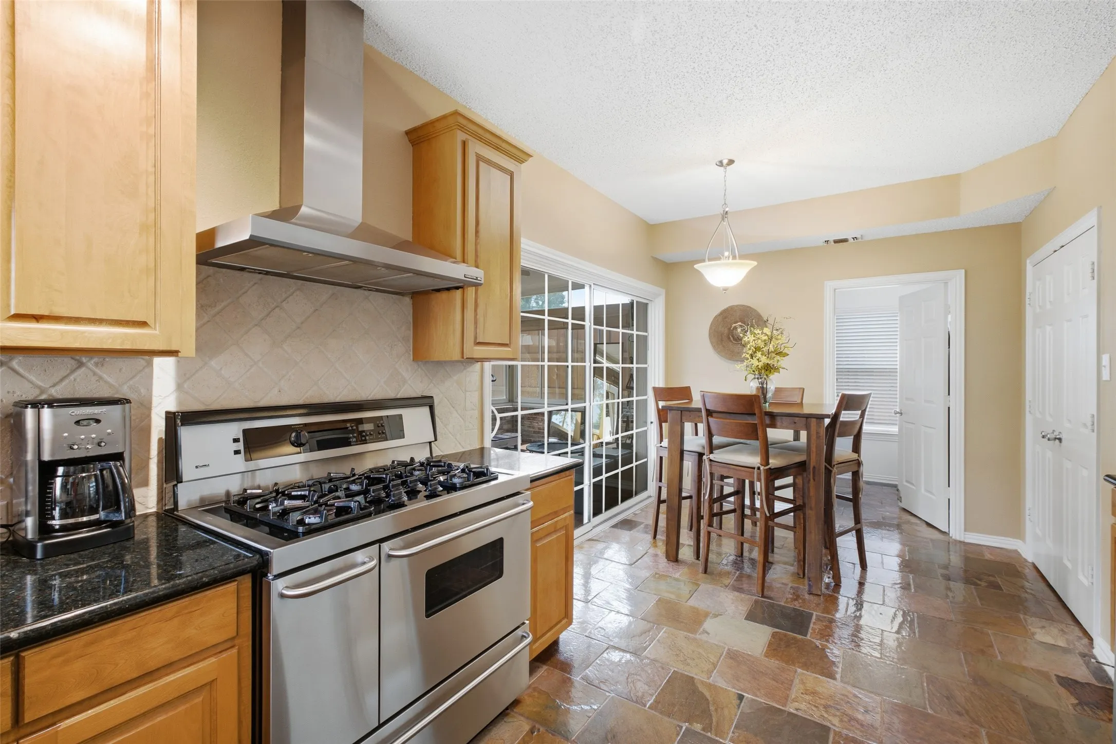 Kitchen with stainless gas range, custom ventilation hood, granite counters, and an adjacent breakfast nook with sliding glass doors to the backyard.