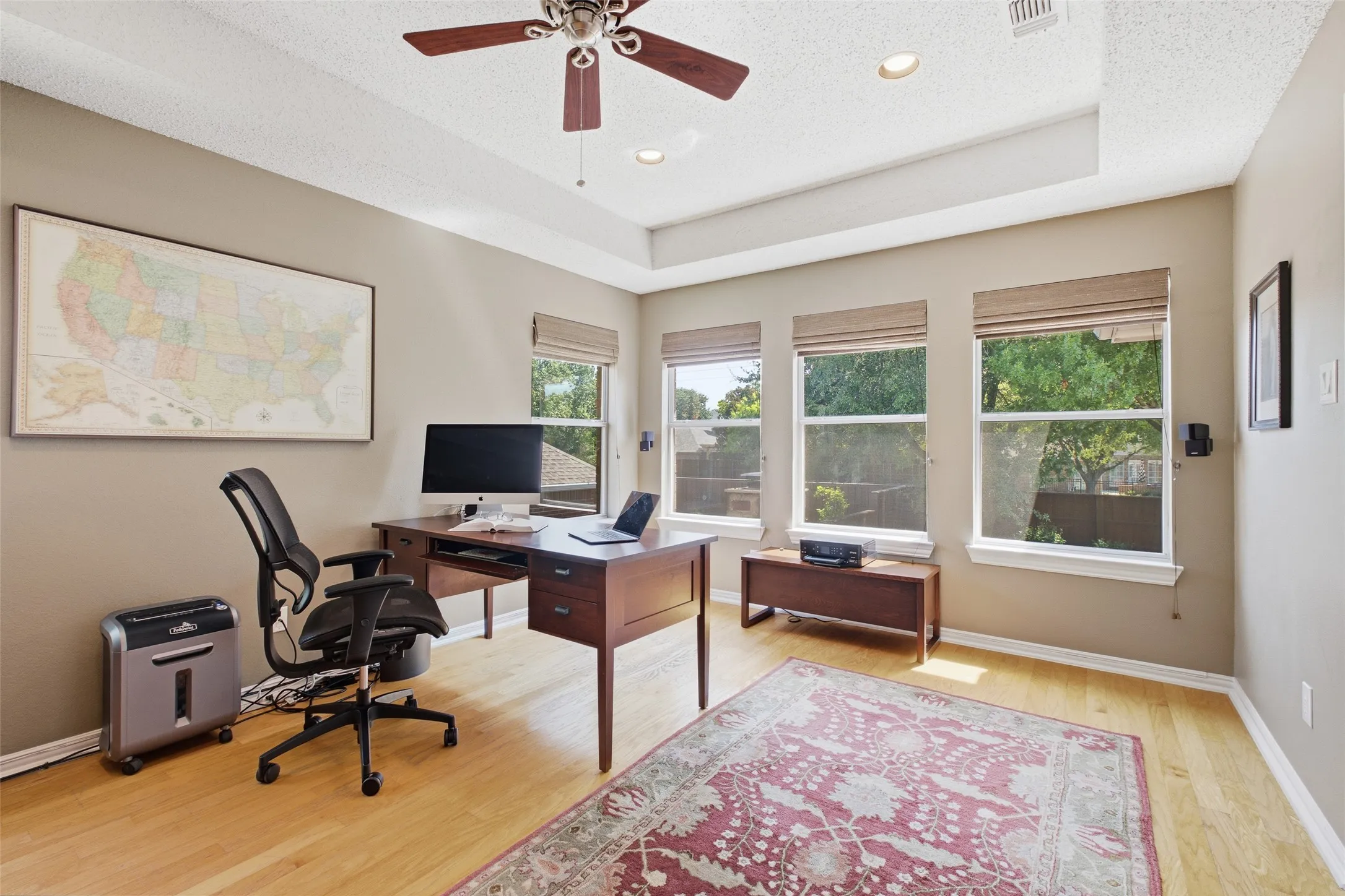 Private home office with a tray ceiling, large windows, hardwood floors, and ample workspace — ideal for working from home in style.