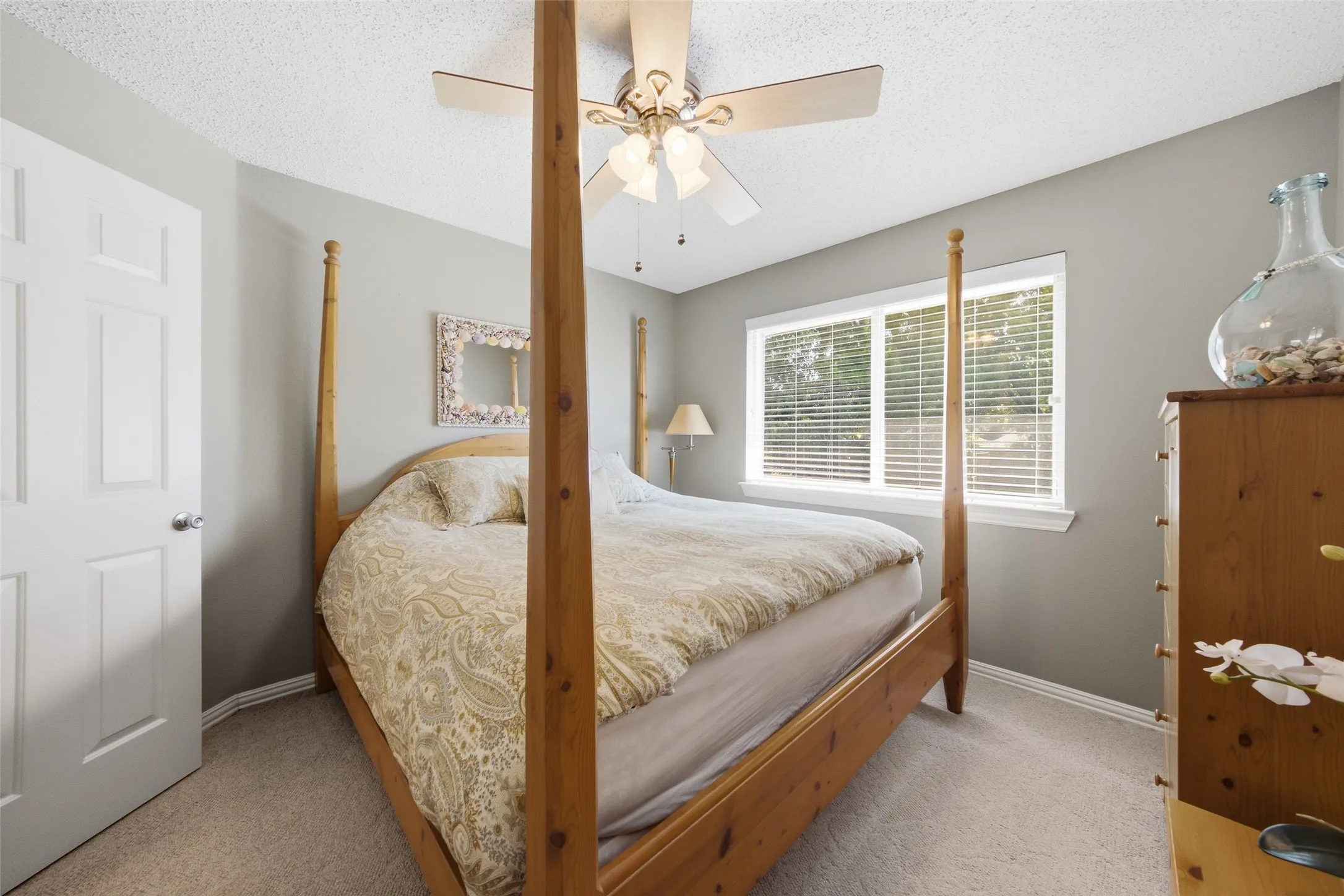 Secondary bedroom with four-poster bed, plush carpet, ceiling fan, and comfortable natural light — a welcoming space for family or guests.