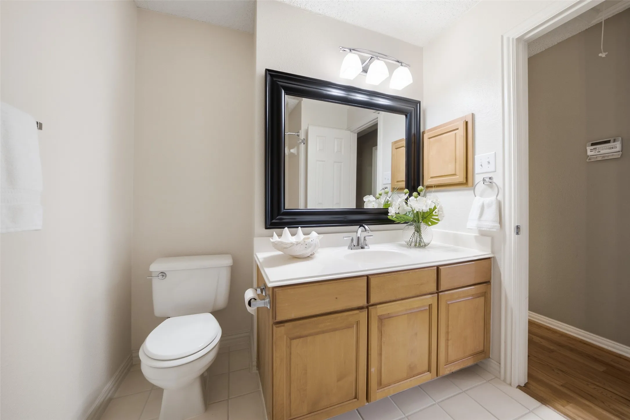 Well-appointed secondary bathroom with single vanity, wood cabinetry, granite countertop, and a stylish black-framed mirror.