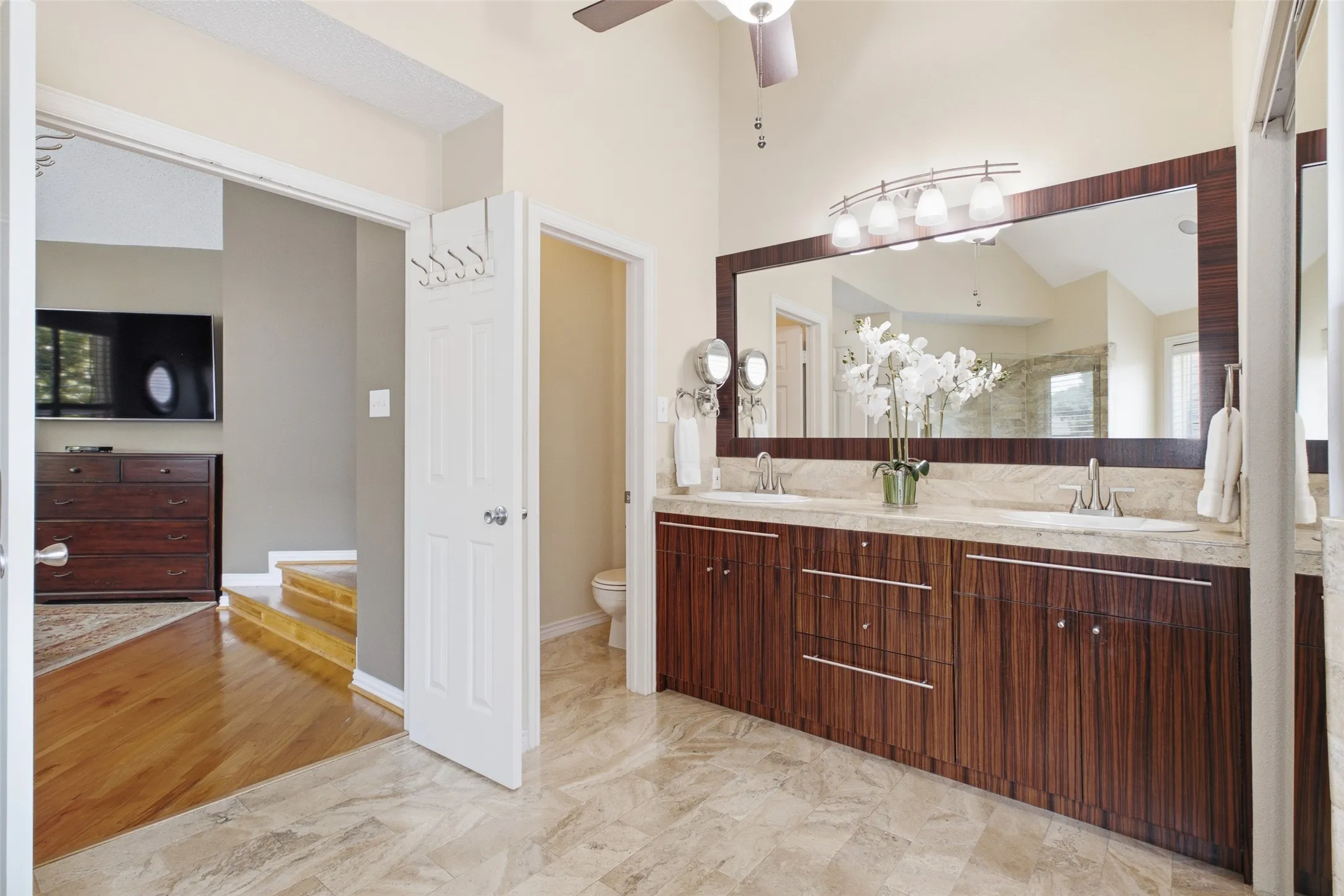 Primary bathroom with dual vanity, granite countertops, custom dark wood cabinetry, a large framed mirror, and direct en-suite access to the bedroom.