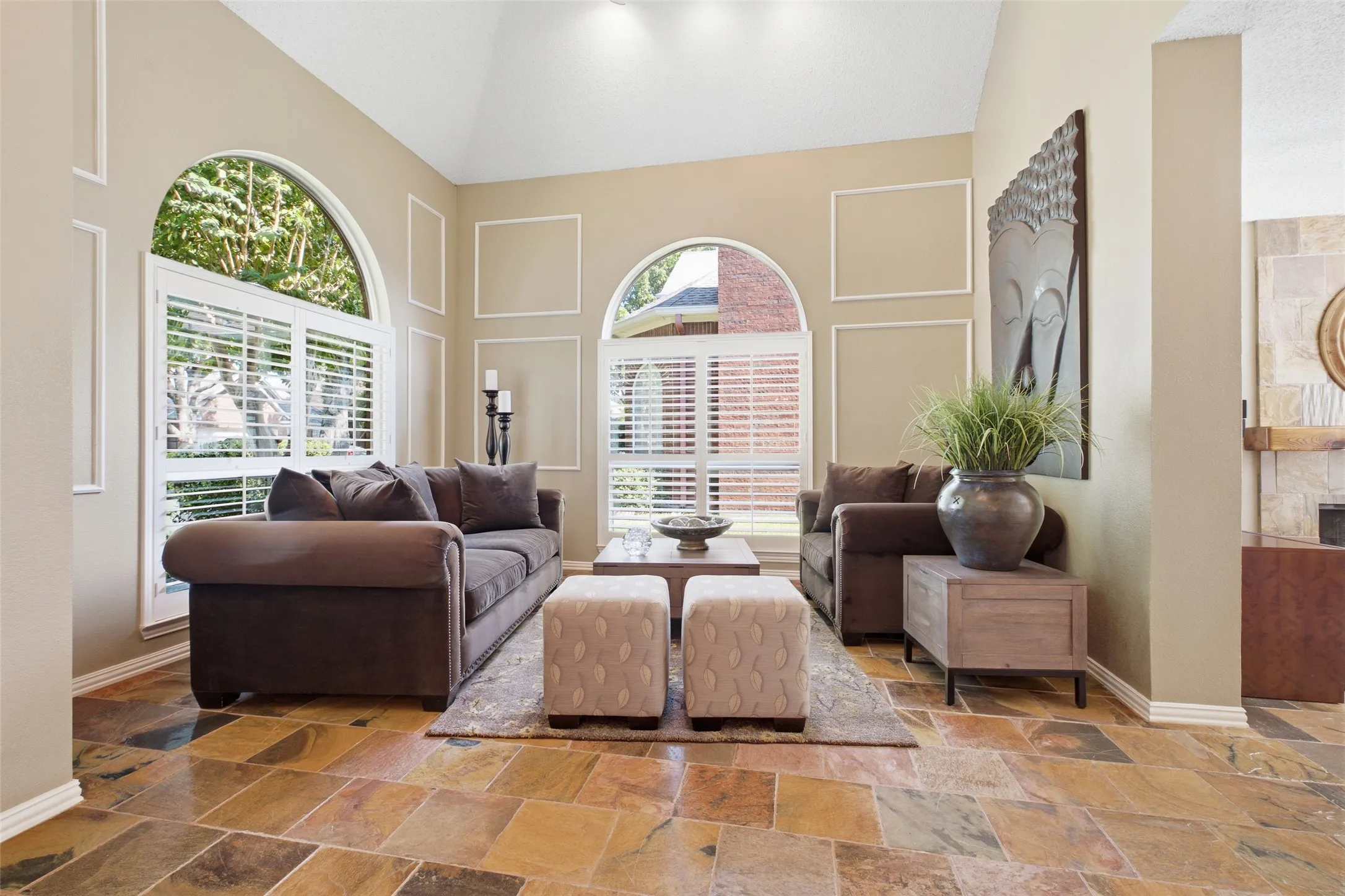Light-filled formal living room with soaring vaulted ceilings, dual arched windows with plantation shutters, and refined wall paneling detail.