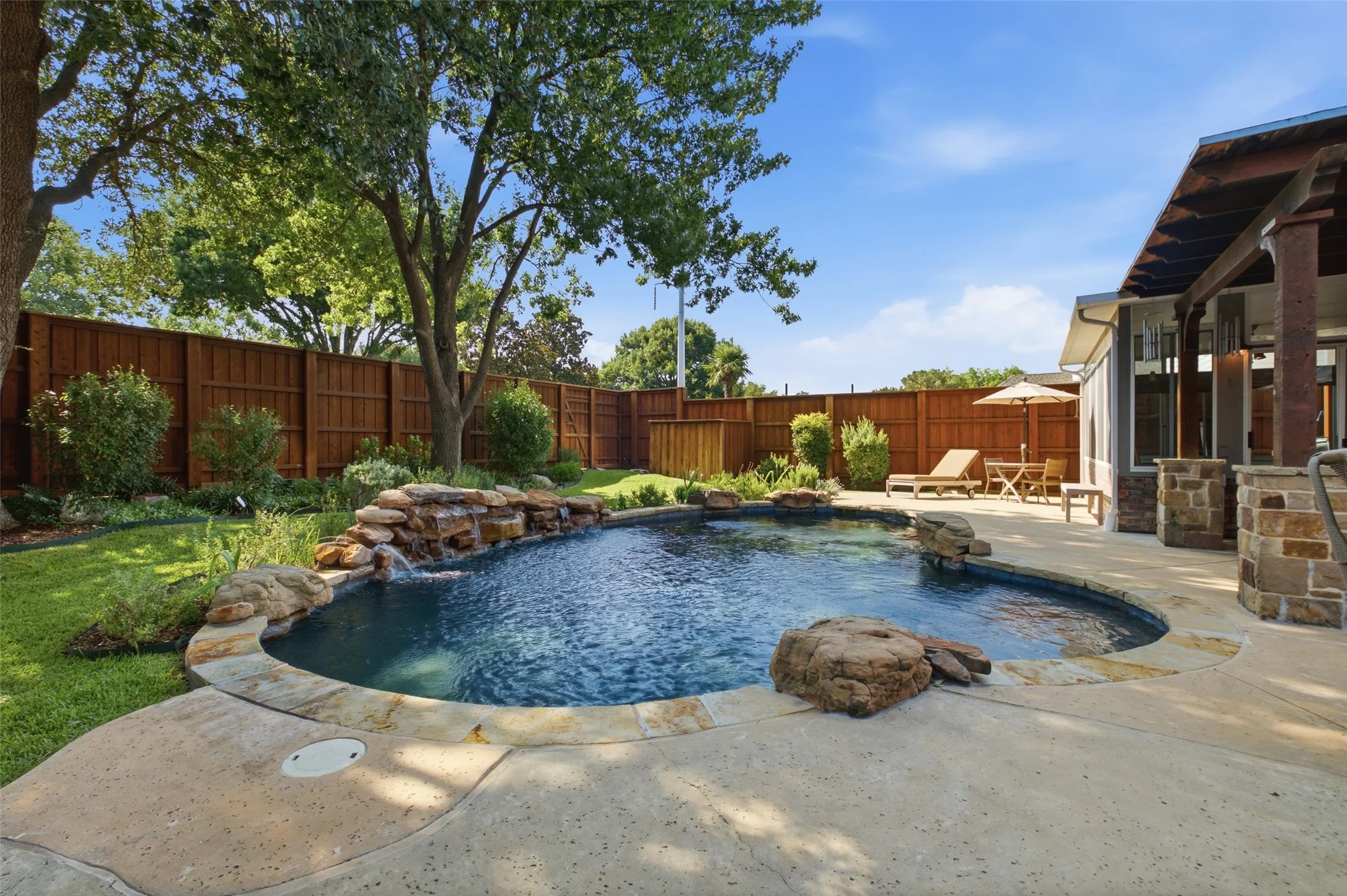 Freeform pool with dual natural rock waterfall features, mature shade trees, and an expansive flagstone patio — a true backyard oasis.