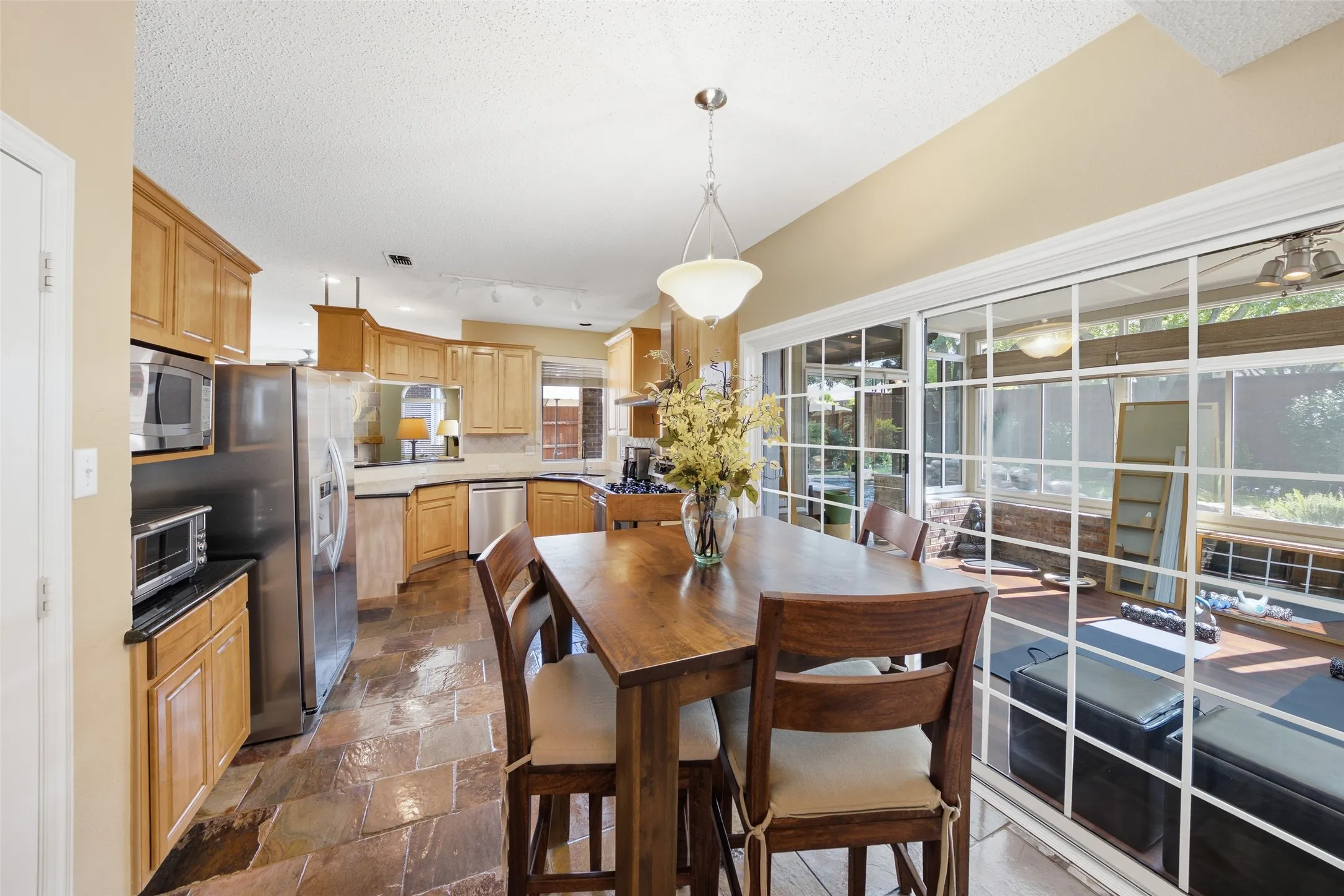 Bright eat-in kitchen with dining area and sweeping views into the sunroom and backyard through large glass windows — the heart of everyday family life.