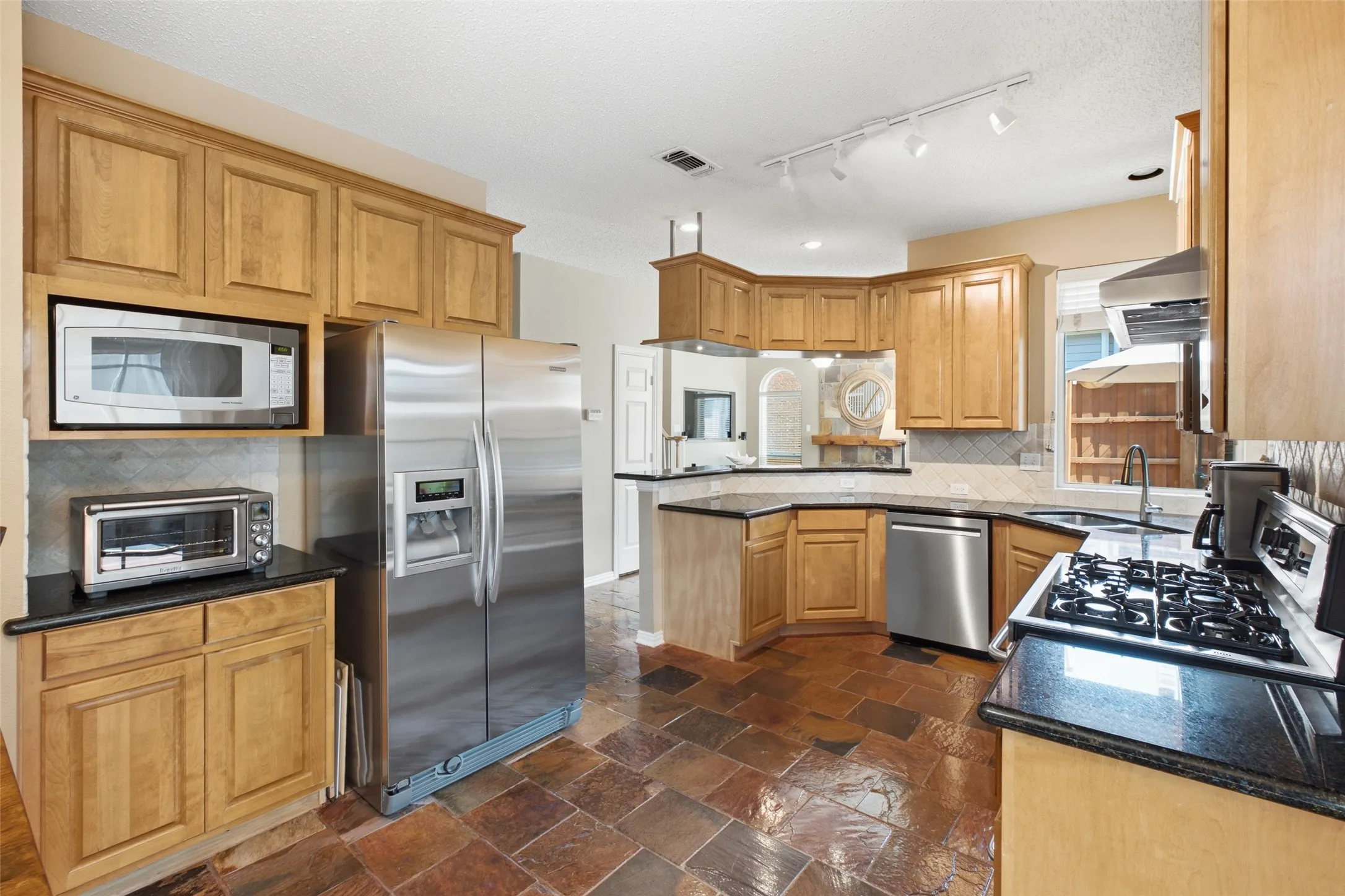 Generously sized kitchen with stainless steel refrigerator, built-in microwave, gas cooktop, dishwasher, and abundant cabinet storage throughout.
