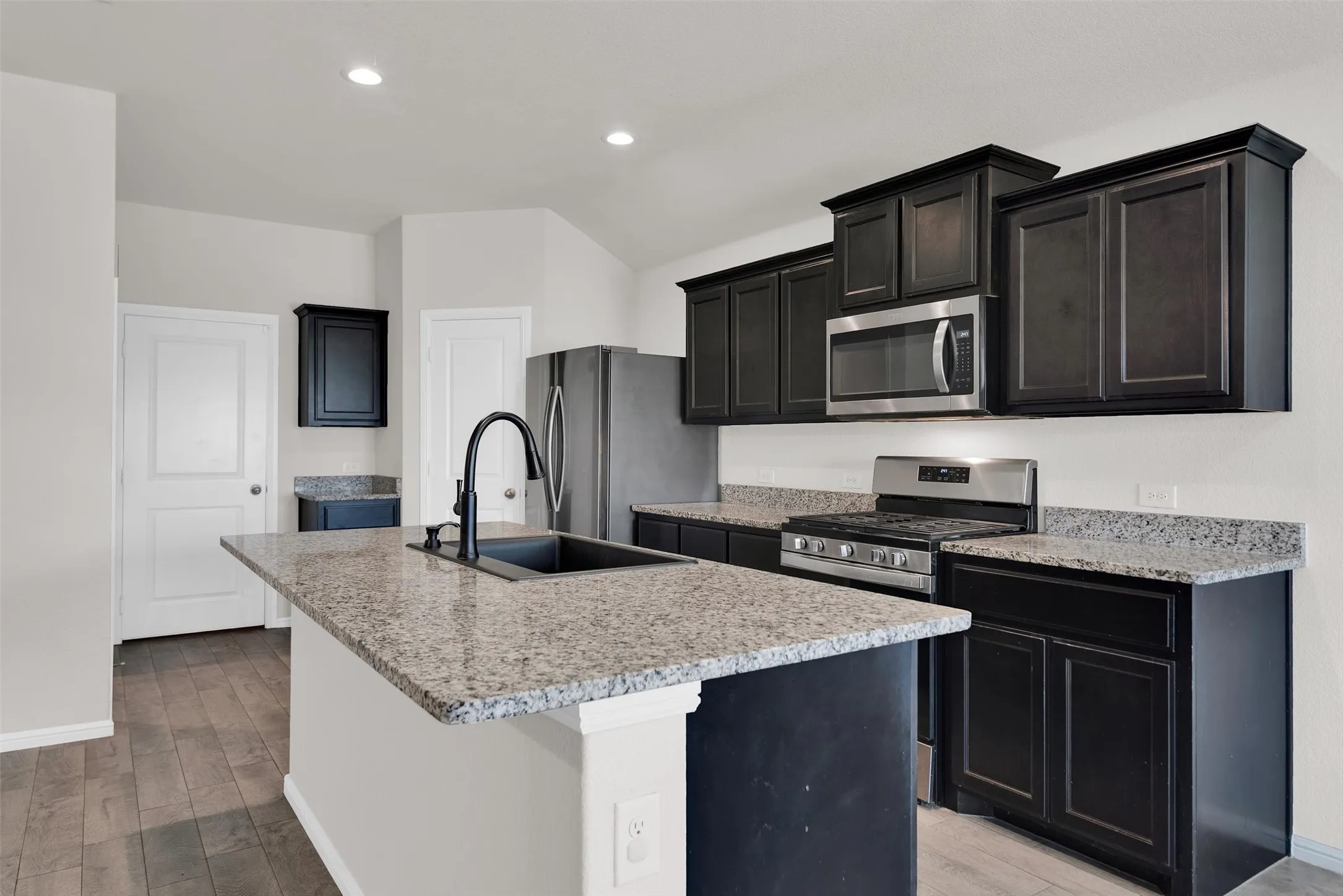 Kitchen featuring dark wood-finish cabinetry, granite countertops, stainless steel appliances, a kitchen island with sink, and recessed lighting