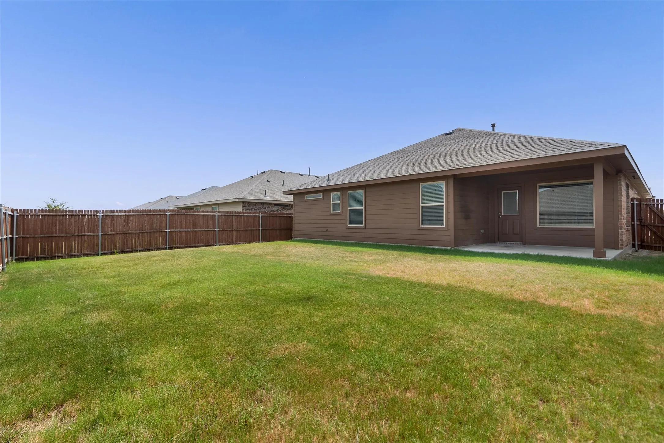 Expansive backyard featuring a privacy fence, covered patio, and brown siding