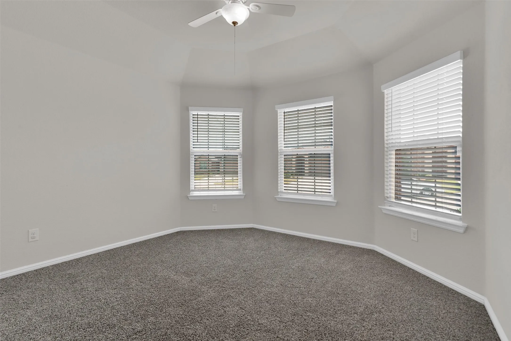 Tray ceiling with ceiling fan, multiple windows with blinds, and neutral tone carpet flooring