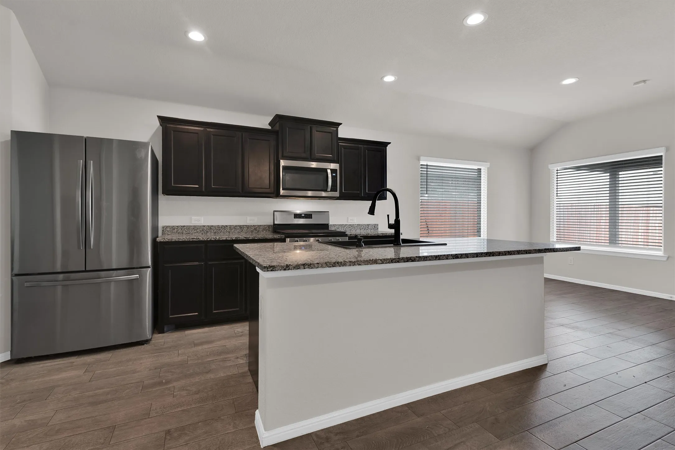 Kitchen featuring dark wood cabinetry, granite countertops, stainless steel appliances, and wood-look tile flooring