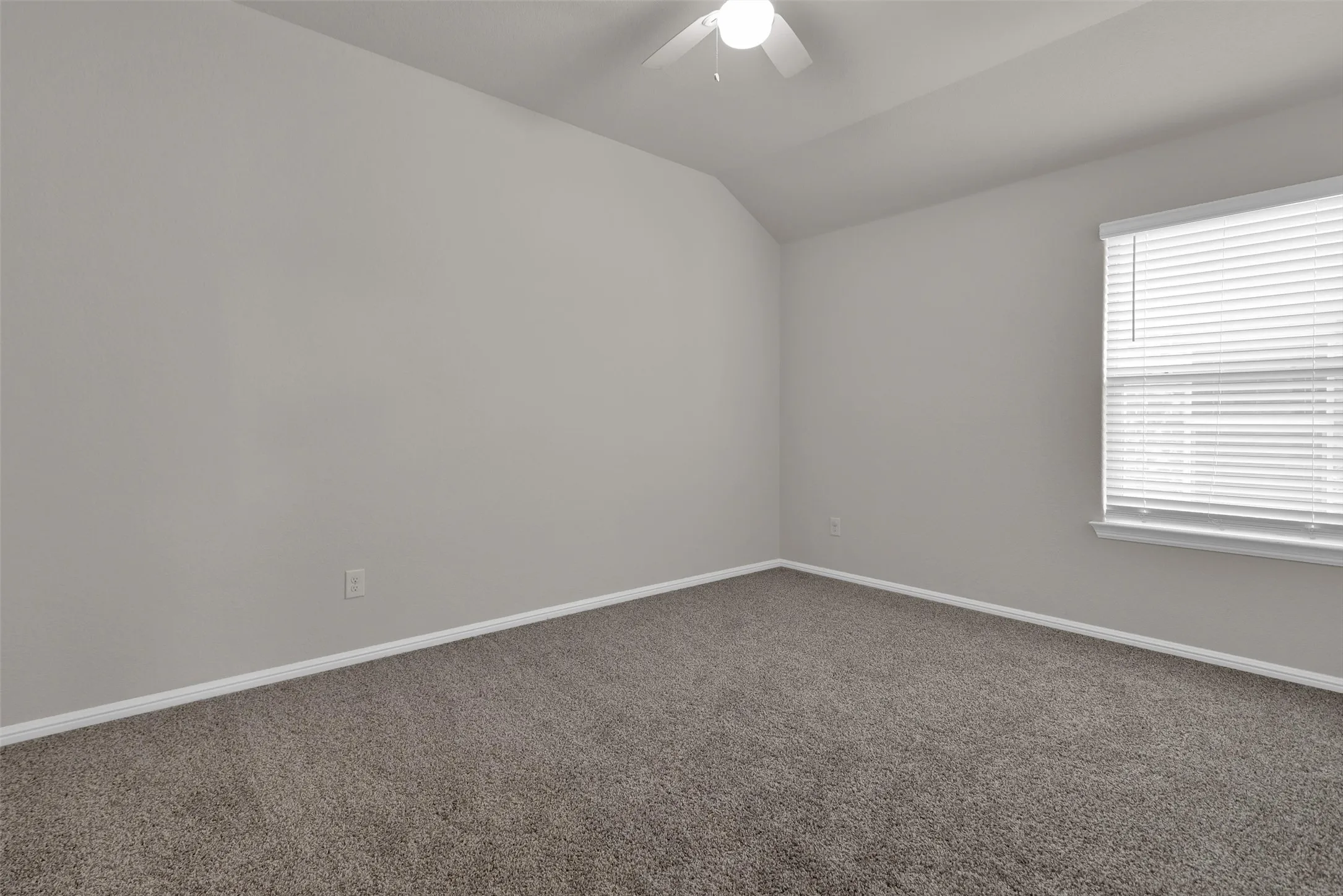 Vaulted ceiling with a ceiling fan, neutral wall paint, carpet flooring, and a window with blinds