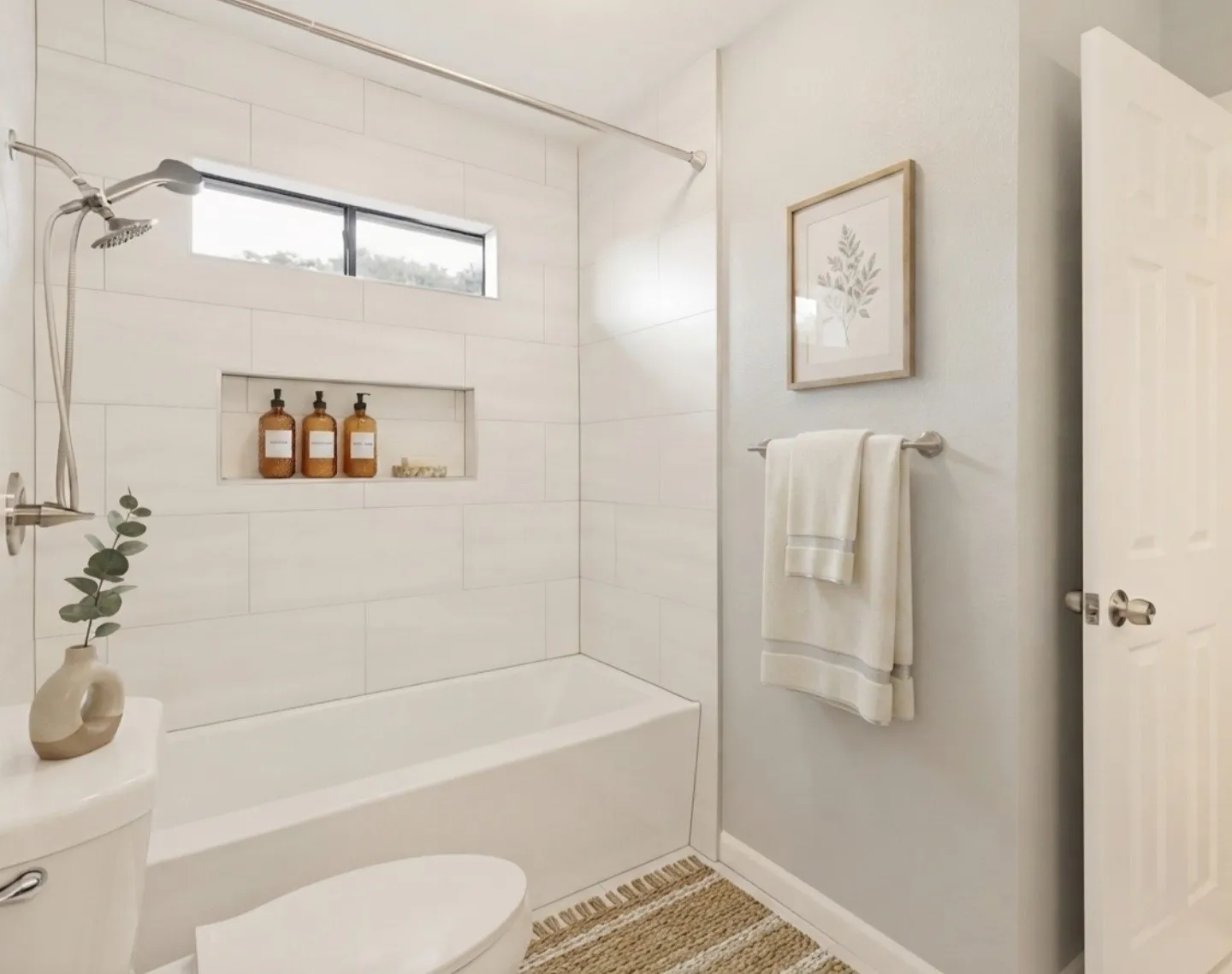 This secondary full bathroom features a clean, modern design with a built-in cubby hole inside the shower, perfect for keeping toiletries organized and within easy reach. A thoughtfully placed window brings in natural light, brightening the space and adding a fresh, airy feel. The bathtub-and-shower combination showcases sleek tilework and contemporary fixtures, while the open doorway leads seamlessly into the adjacent bedroom. This bathroom is both functional and stylish, offering everyday comfort with smart storage and a bright, welcoming layout.