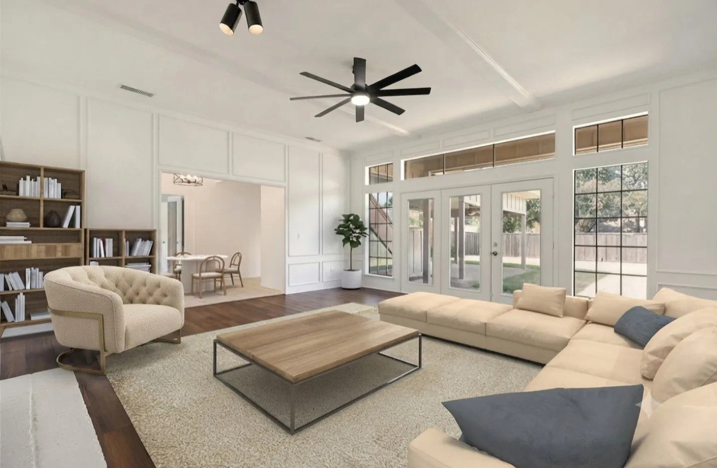 This inviting living area showcases a beautifully maintained interior with fresh paint and professionally cleaned surfaces that give the space a crisp, polished feel. Large windows and glass doors fill the room with natural light and offer a clear view of the expansive backyard, creating a seamless connection between indoor comfort and outdoor space. The lovely flooring adds richness and contrast against the bright walls, while the ceiling fan and lighting enhance the room’s functionality. The wide opening into the adjacent area highlights the home’s generous layout and easy flow, making everyday living feel open, comfortable, and effortless.
