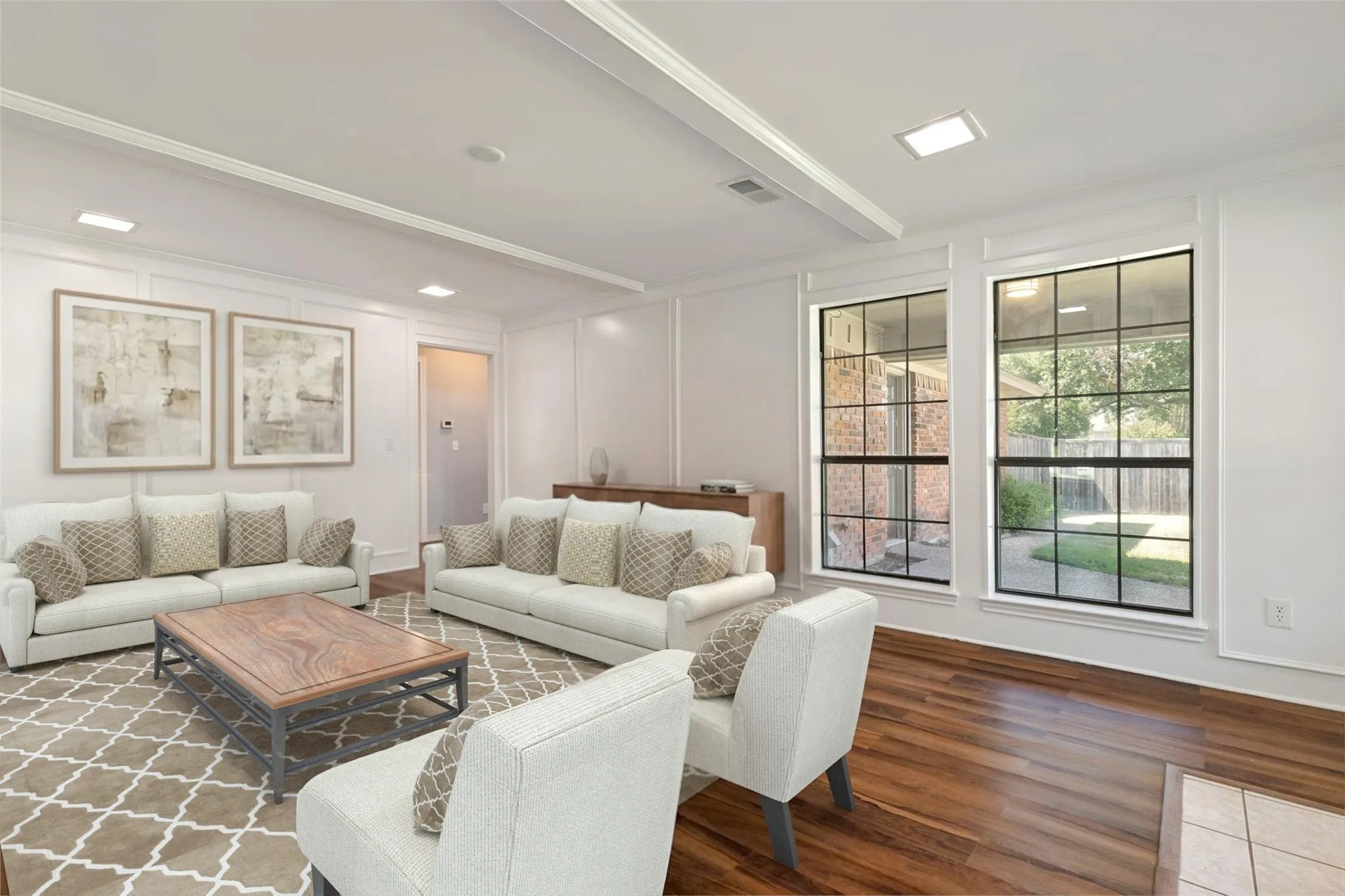 This beautifully designed room afeatures decorative ceiling beams and recessed lighting that add architectural interest and a polished, modern touch. The pair of large windows create a striking visual contrast and offer a clear, framed view of the outdoor space, bringing in balanced natural light. The dark flooring grounds the room with richness, while the bright walls keep the space feeling open and crisp. A clean doorway transition leads into the next area of the home, showcasing thoughtful design and smooth connectivity. This room stands out for its refined ceiling detail and the way it captures the outdoor scenery with style and clarity.