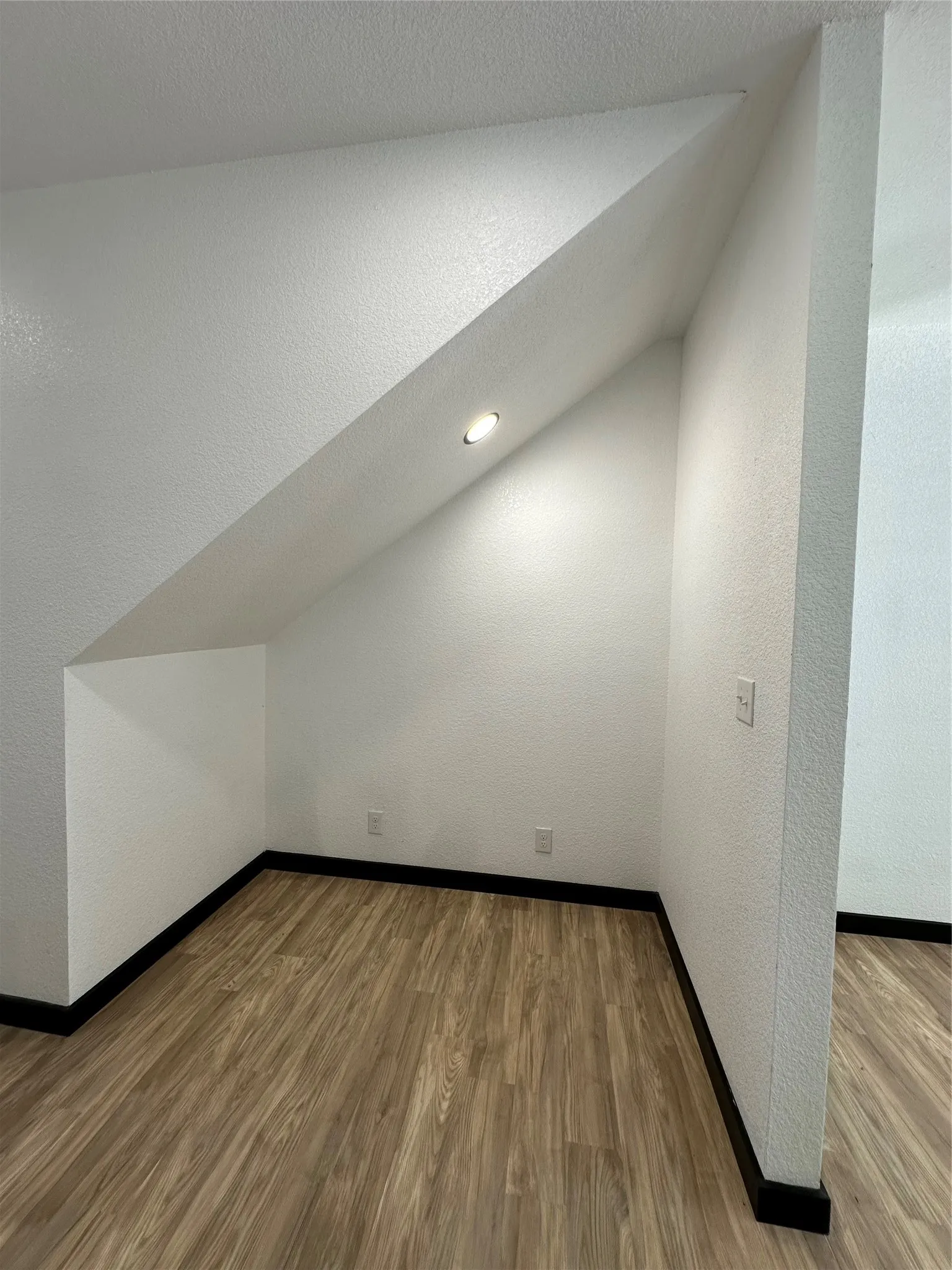 Recessed ceiling lighting, wood-finish flooring, white textured walls, and dark trim