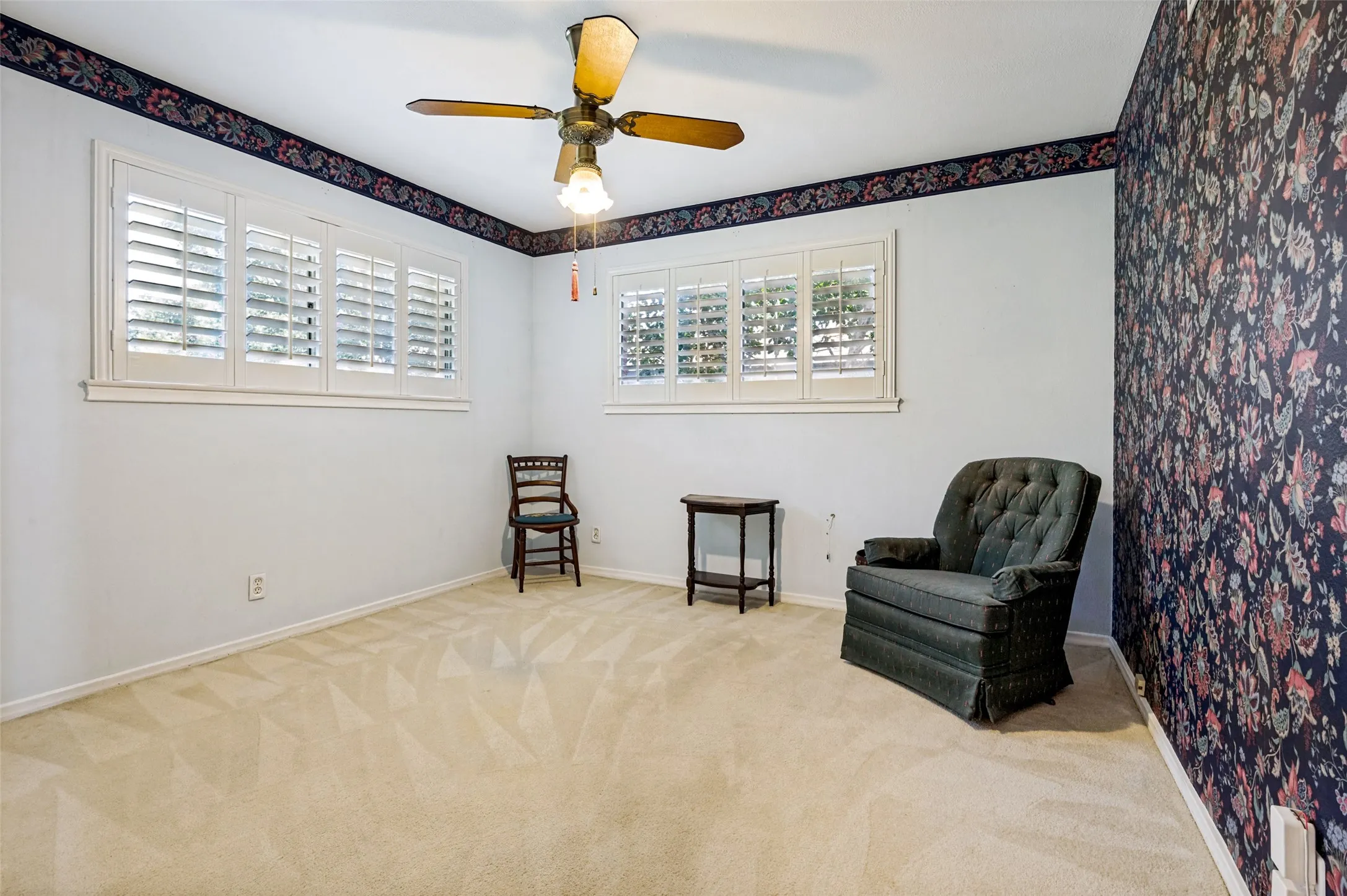 Wall-to-wall carpeting, multiple windows with plantation shutters, ceiling fan with integrated lighting, and a patterned accent wall