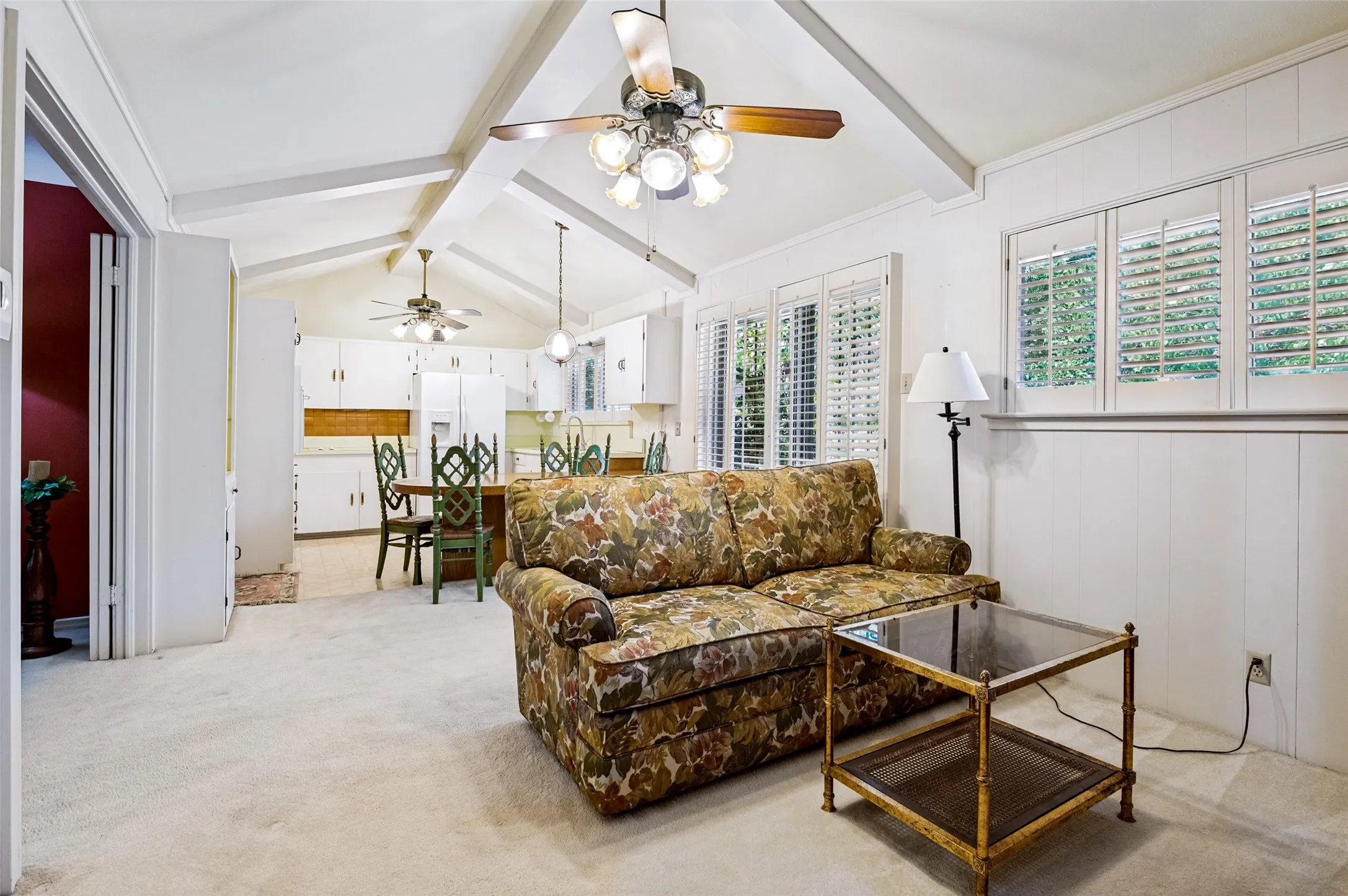 Vaulted ceiling with exposed beams, white paneled walls, and multiple windows with plantation shutters