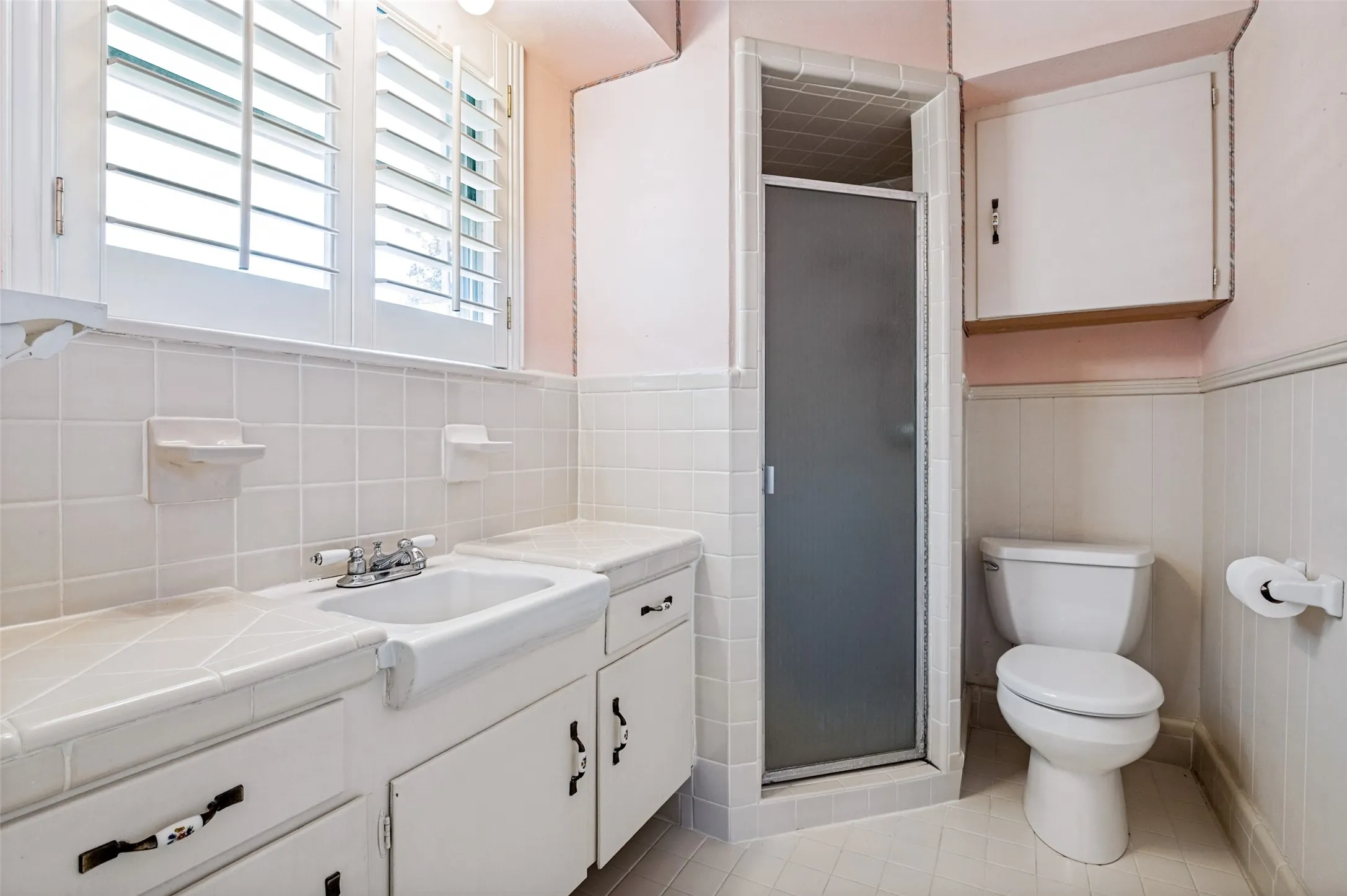 Full bathroom featuring a pedestal sink with chrome faucet, white subway tile wainscoting, toilet with wall-mounted paper holder, and a separate shower enclosure with glass door