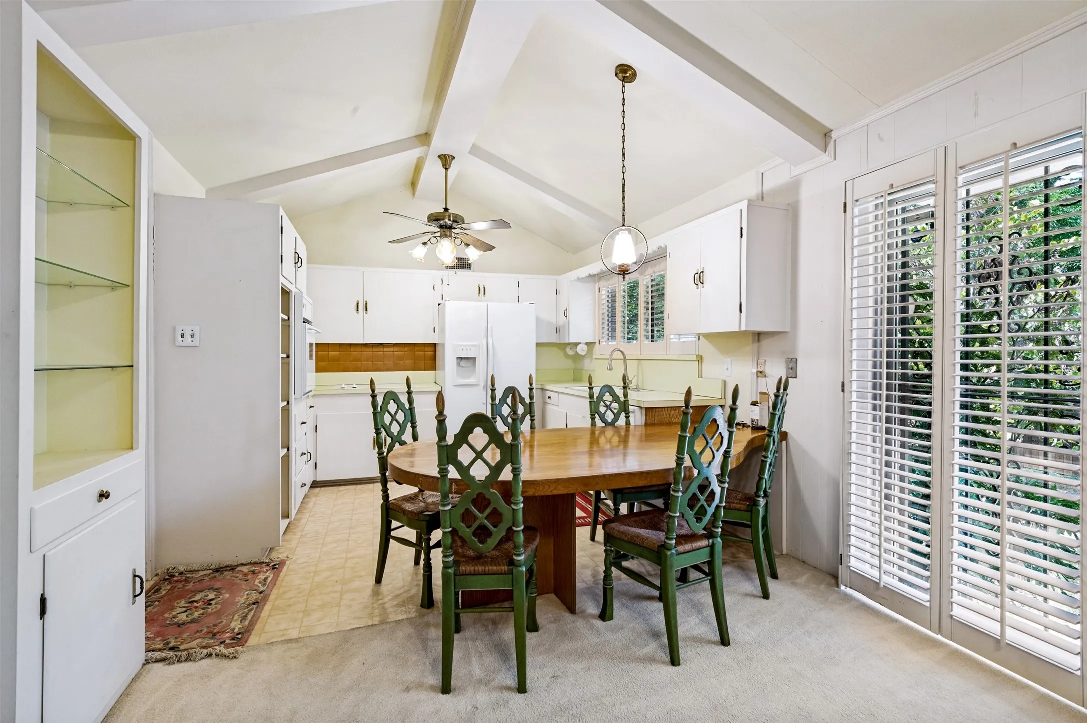 Vaulted ceiling with exposed beams, white cabinetry, integrated glass-front display cabinet, and plantation shutters