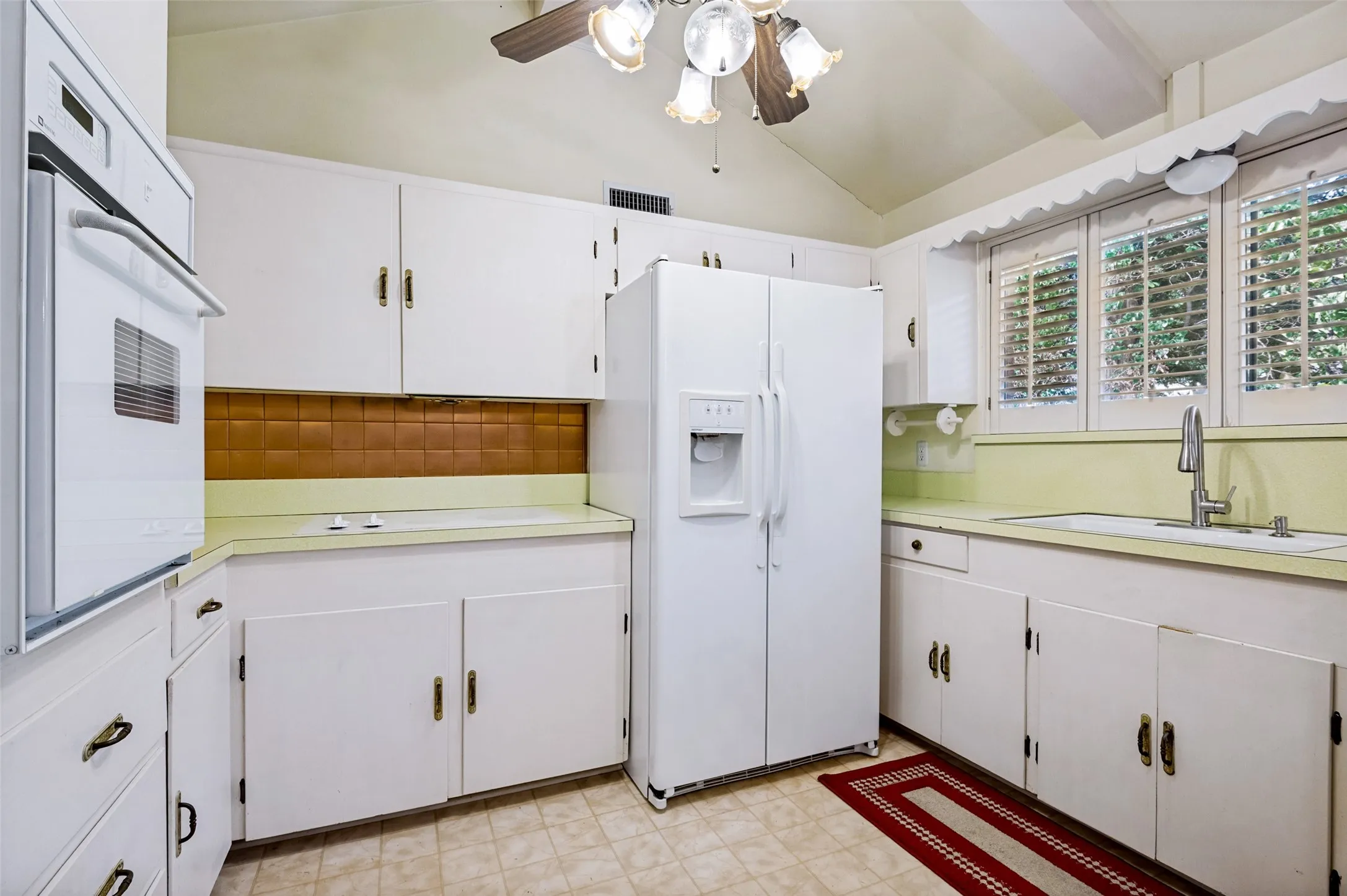 White cabinetry with brass-finish hardware, built-in wall oven, and a double-door refrigerator