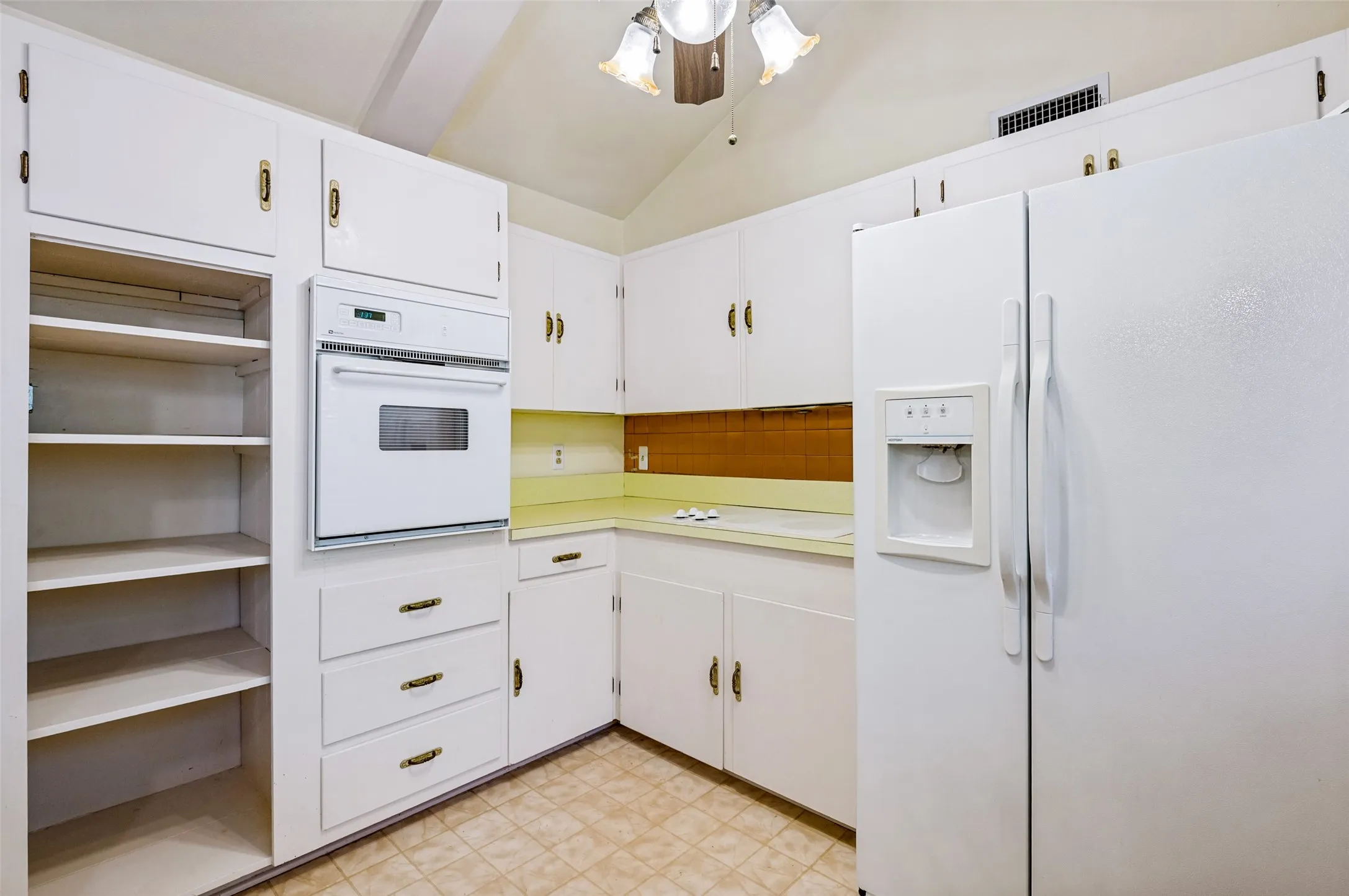 Built-in oven, white cabinetry, light-colored countertops, tile flooring, and integrated refrigerator