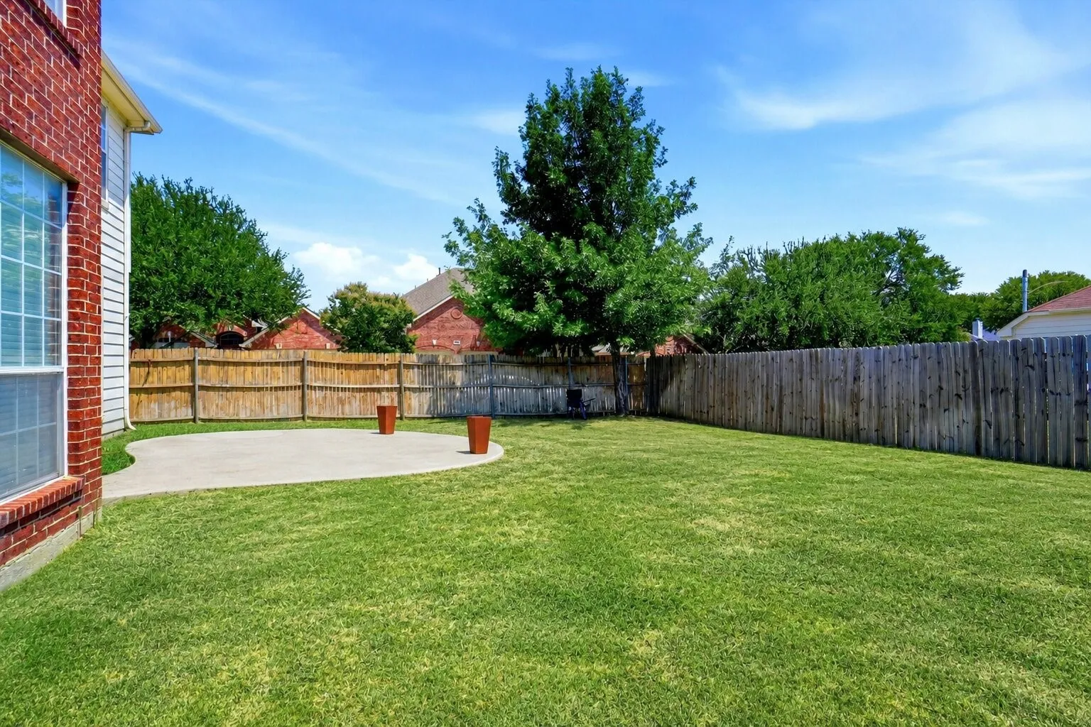 Alternate backyard view showcasing the expansive lawn, mature shade tree, and additional concrete slab—ideal for a future seating or firepit area.