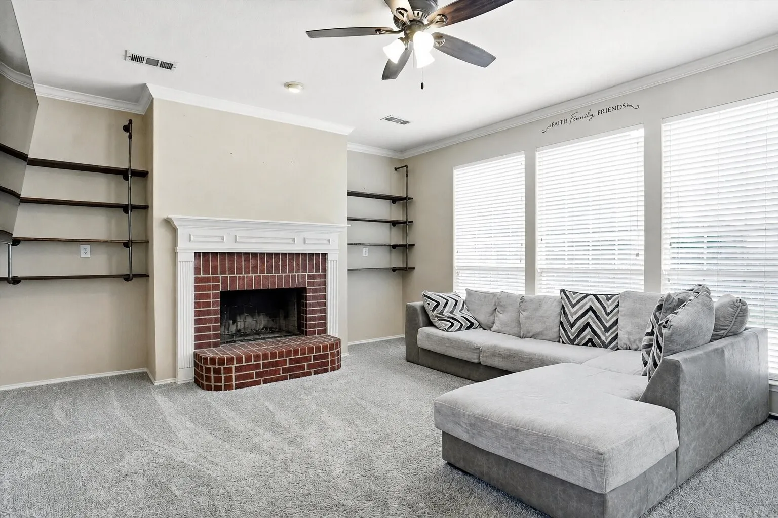 Spacious living room featuring a brick fireplace, custom built-in shelving, crown molding, and abundant natural light from multiple windows.