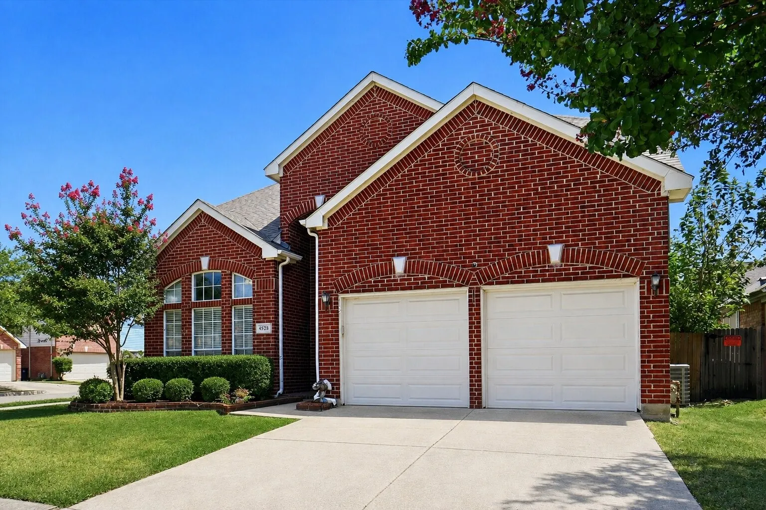 Alternate front exterior angle showcasing the spacious driveway, mature shade trees, and attractive curb appeal.