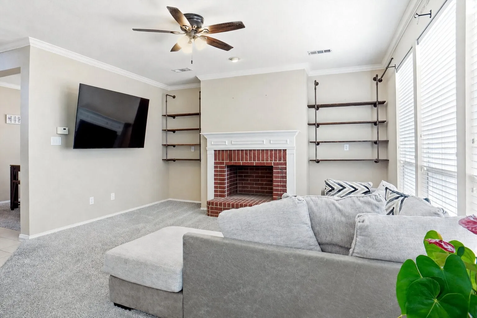 Alternate view of the living room highlighting the brick fireplace, built-in shelving, wall of windows, and spacious layout.