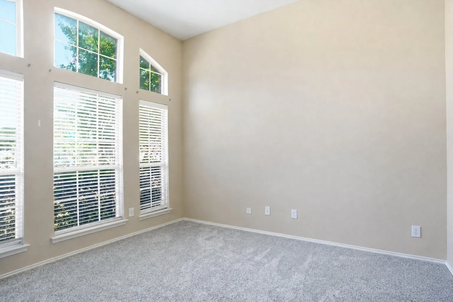 Dedicated home office featuring soaring ceilings, abundant natural light, and a dramatic wall of windows.