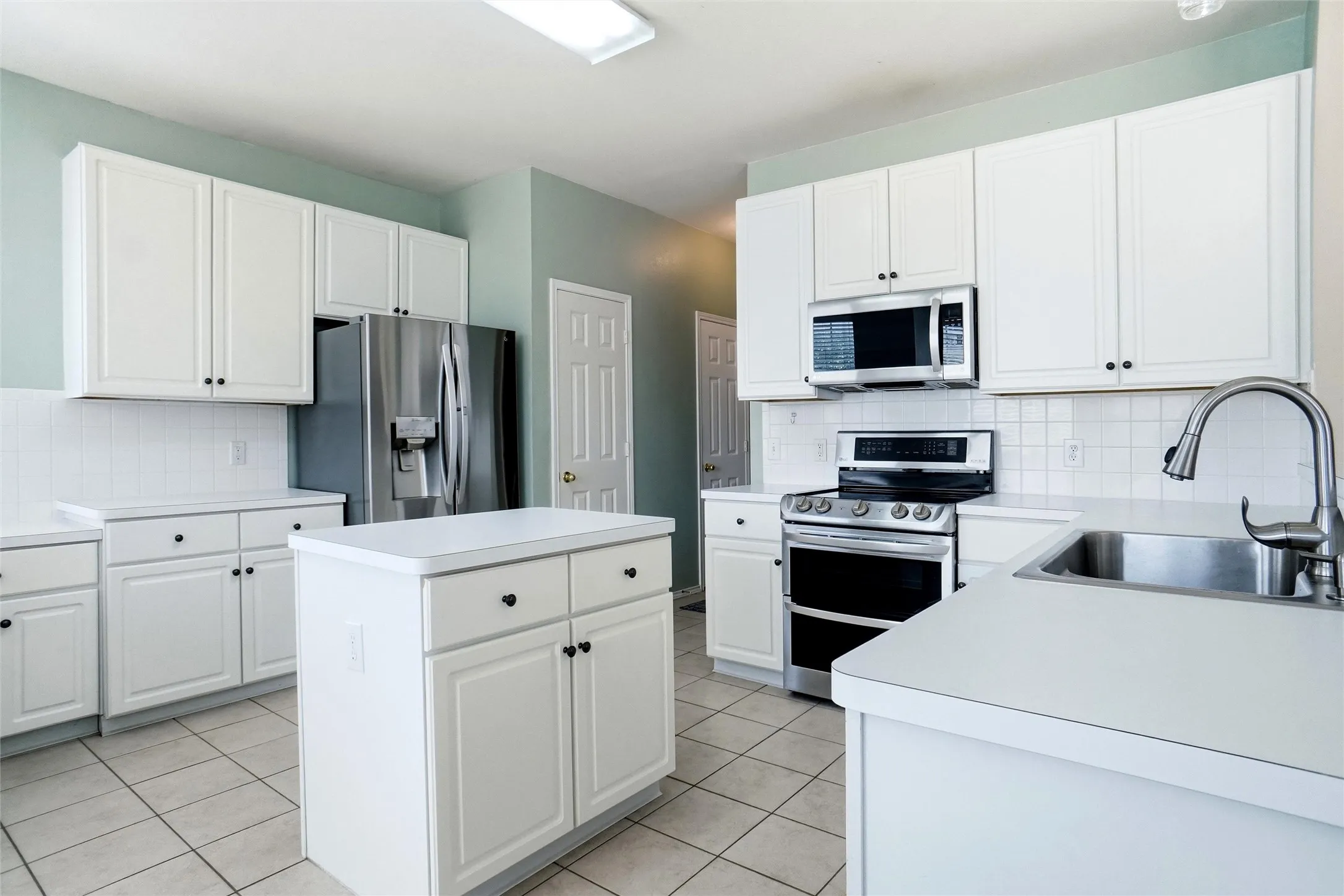 Alternate kitchen view showcasing the center island, abundant white cabinetry, stainless steel appliances, and generous counter space.