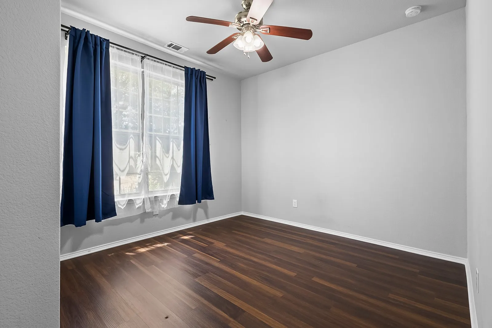 Room featuring wood-finish flooring, light grey walls, and a ceiling fan with integrated lighting