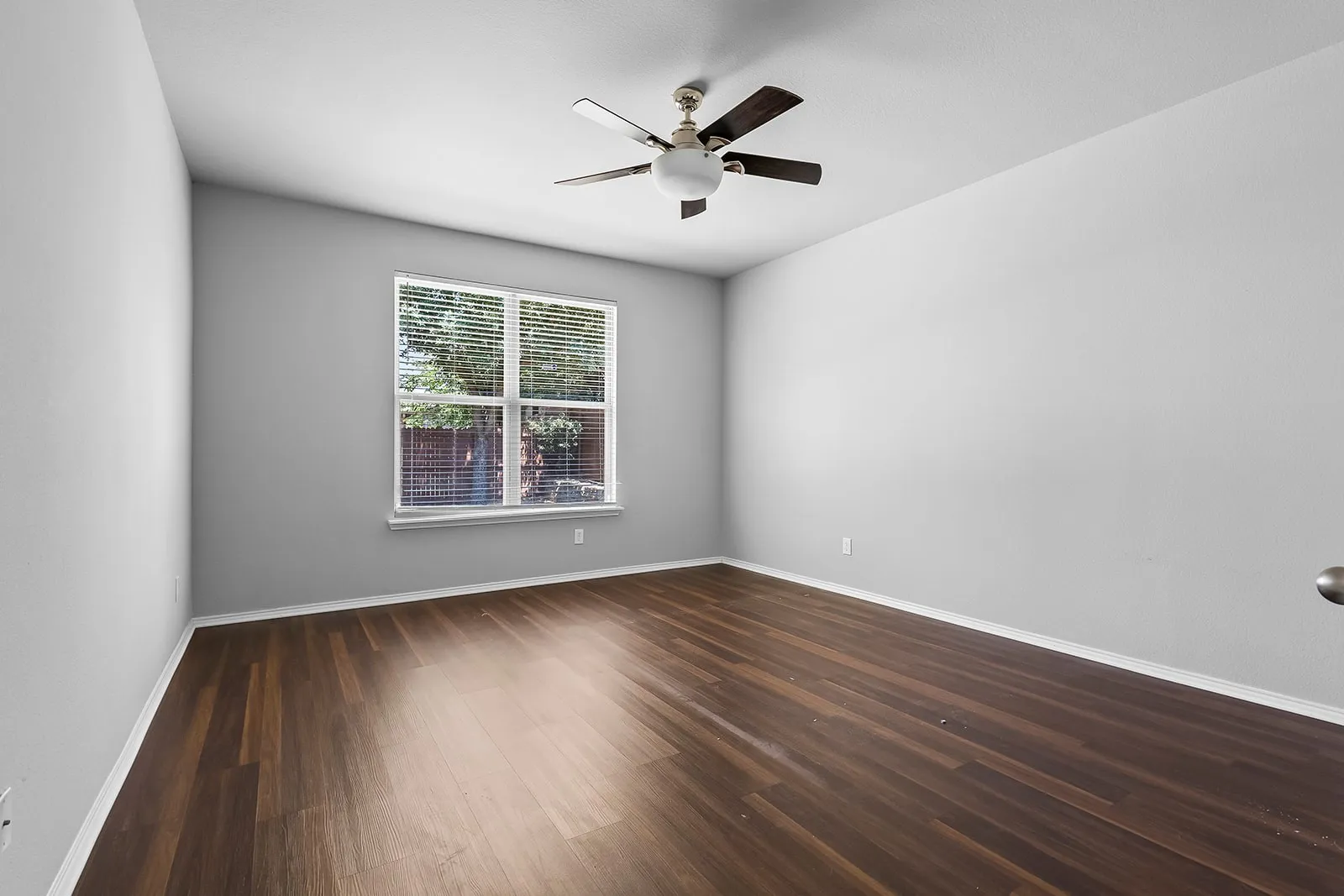 Spacious room featuring wood-finish flooring, light grey walls, and white baseboards
