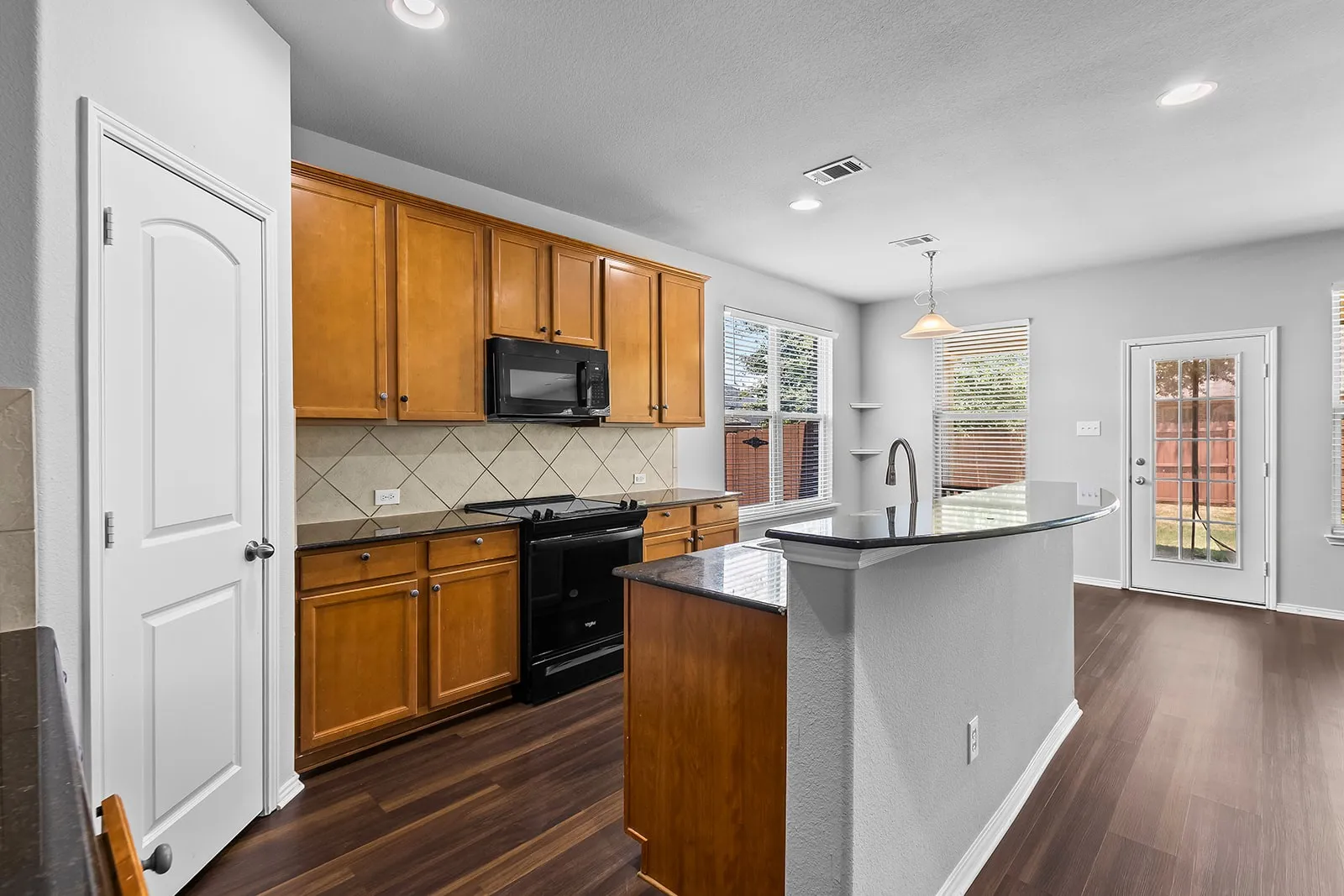 Kitchen featuring rich wood cabinetry, black appliances, a tiled backsplash, wood-finish flooring, and a breakfast bar with a gooseneck faucet