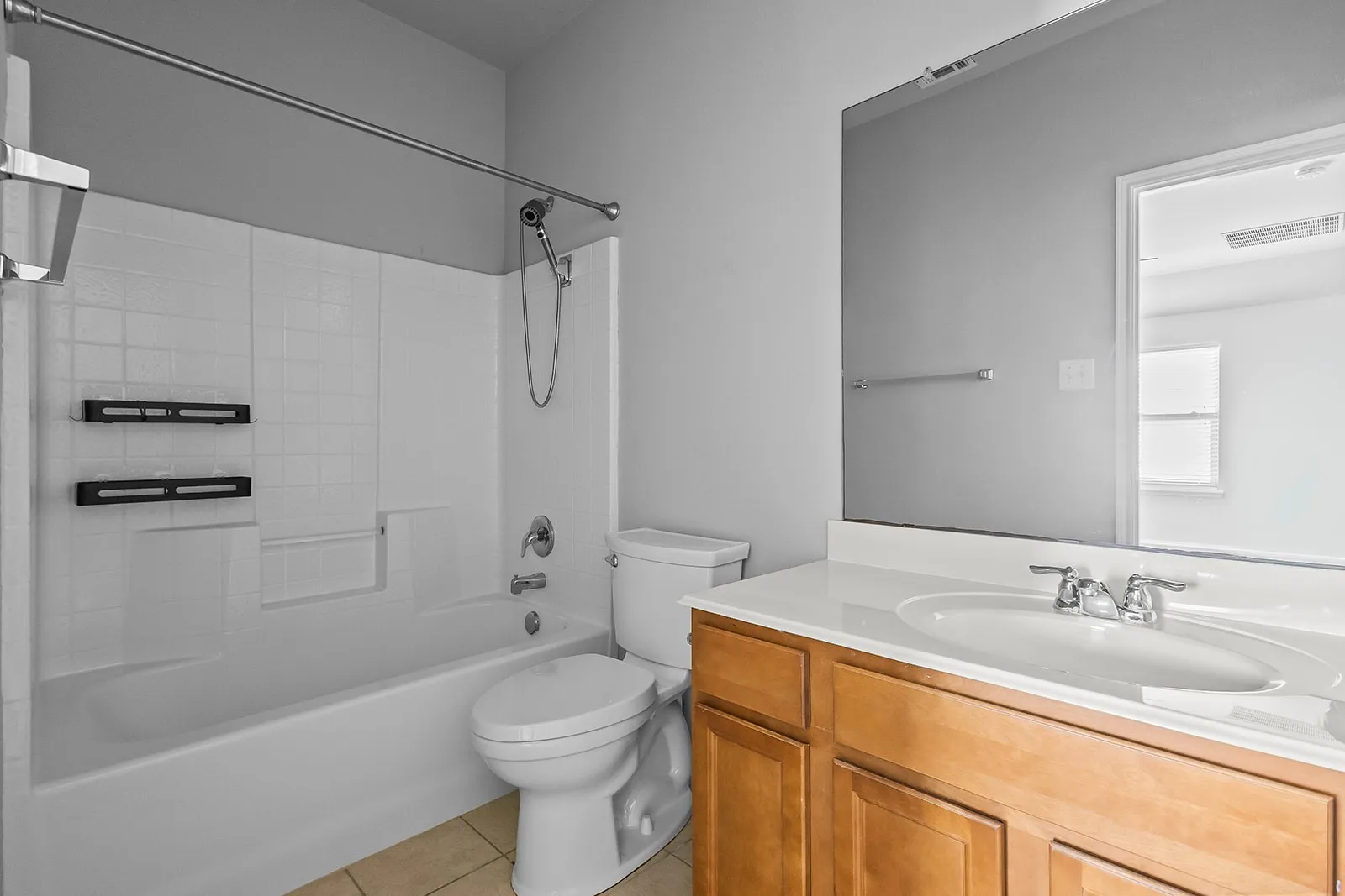 Bathroom featuring a white tub and shower combination with a handheld showerhead, a toilet, a wood-finish vanity with a white countertop, and an integrated sink with a chrome faucet