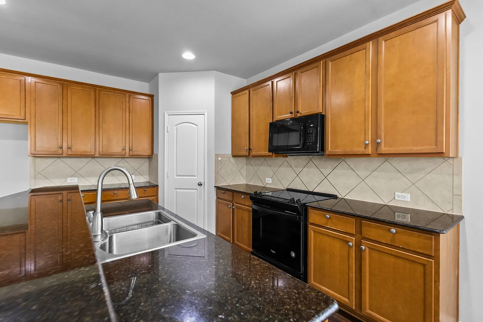 Kitchen featuring a stainless steel undermount sink, a pull-down faucet, granite countertops, wood cabinetry, and a tile backsplash